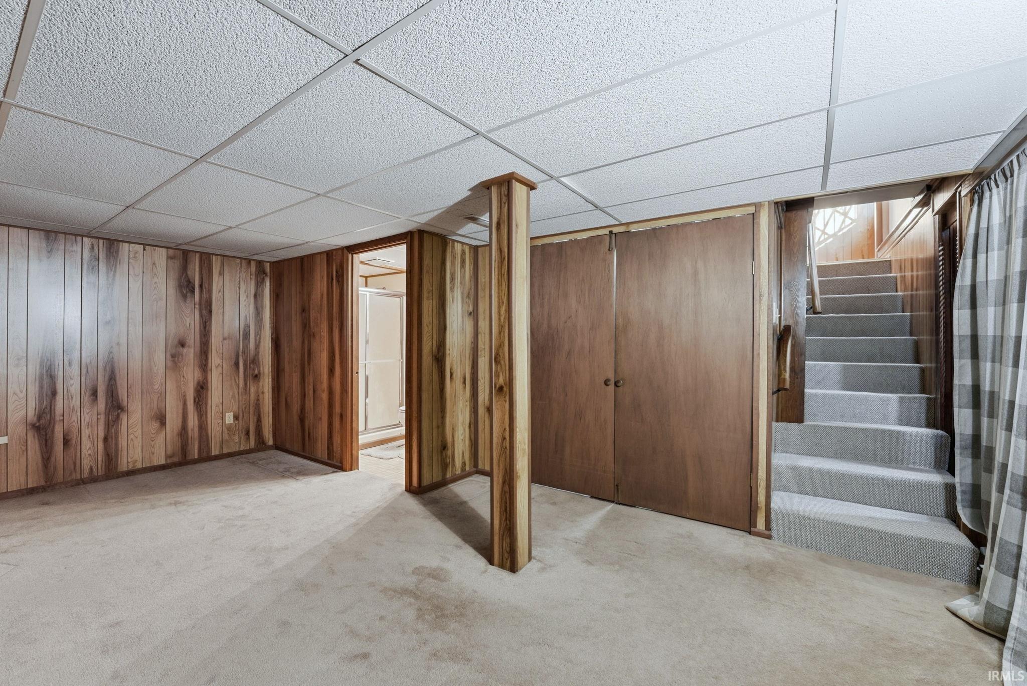 Finished below grade area featuring a drop ceiling, light carpet, and wood walls