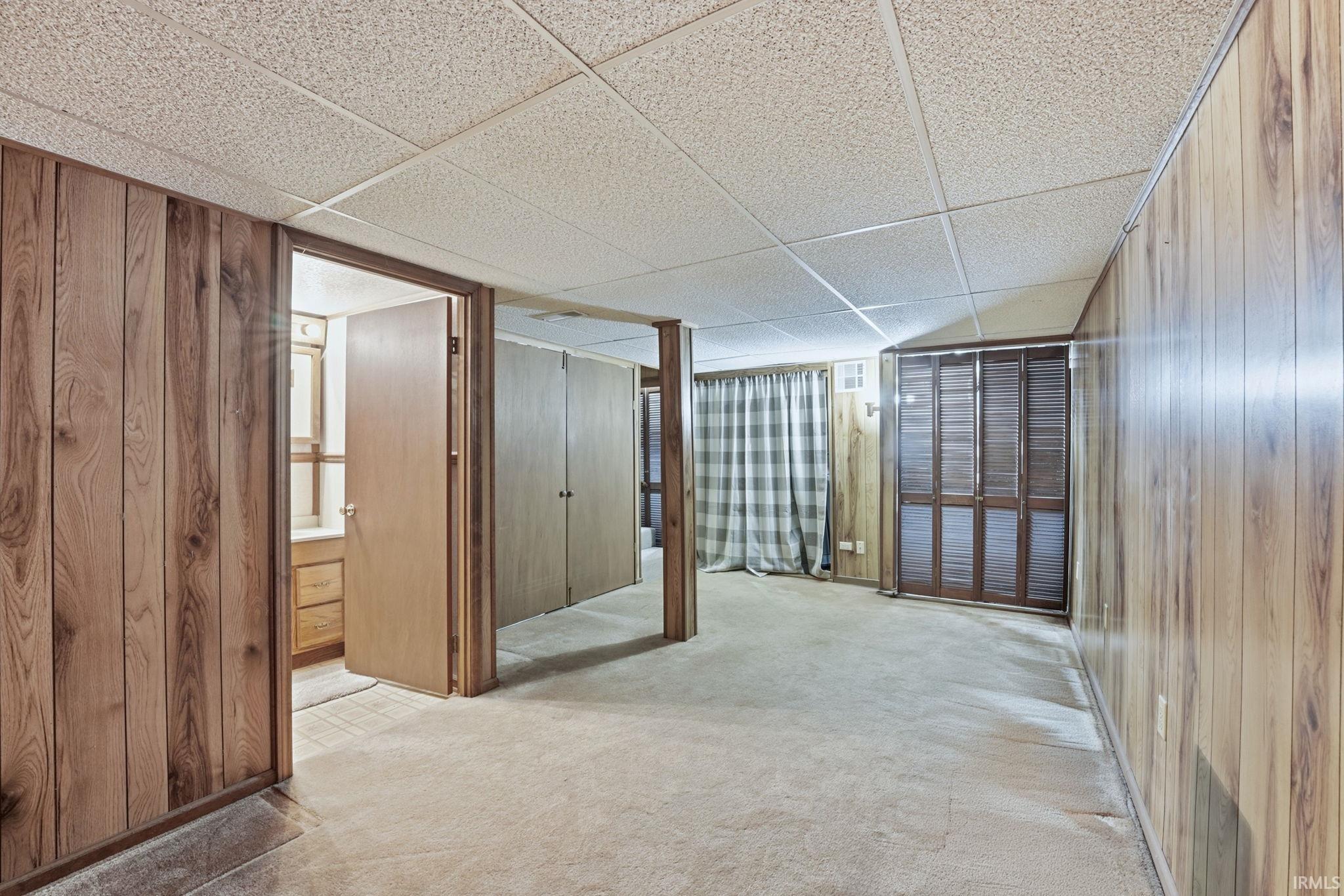 Unfurnished room featuring a paneled ceiling, light colored carpet, and wood walls