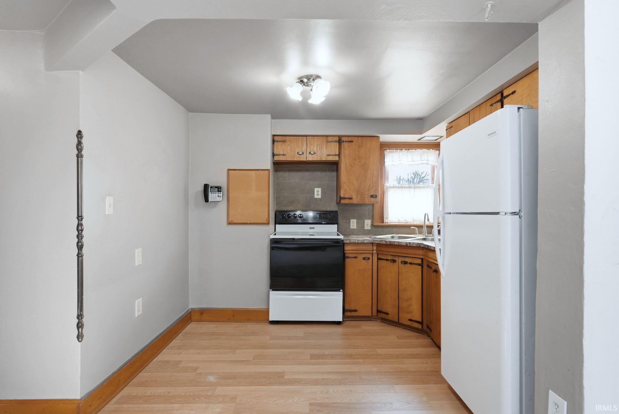 Kitchen featuring white appliances, wood finish cabinets, light wood finished floors, and decorative backsplash
