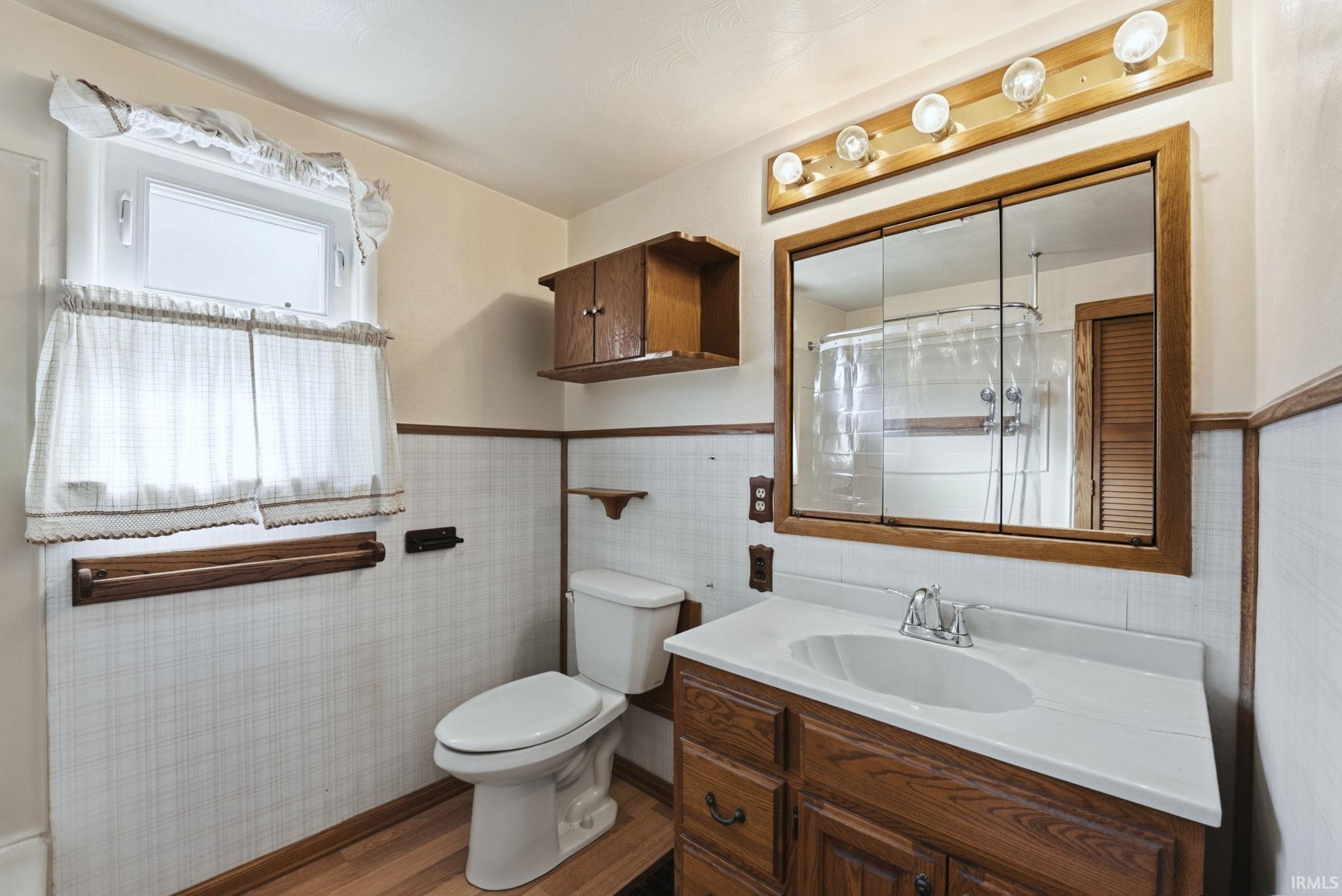 Bathroom featuring vanity, wood finished floors, curtained shower, and a wainscoted wall