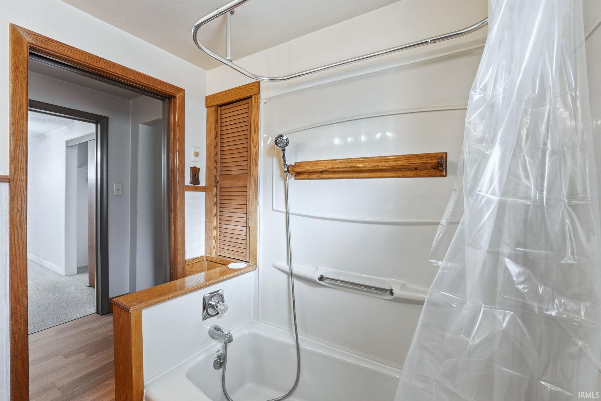 Full bath with light wood finished floors and shower / bath combo with shower curtain