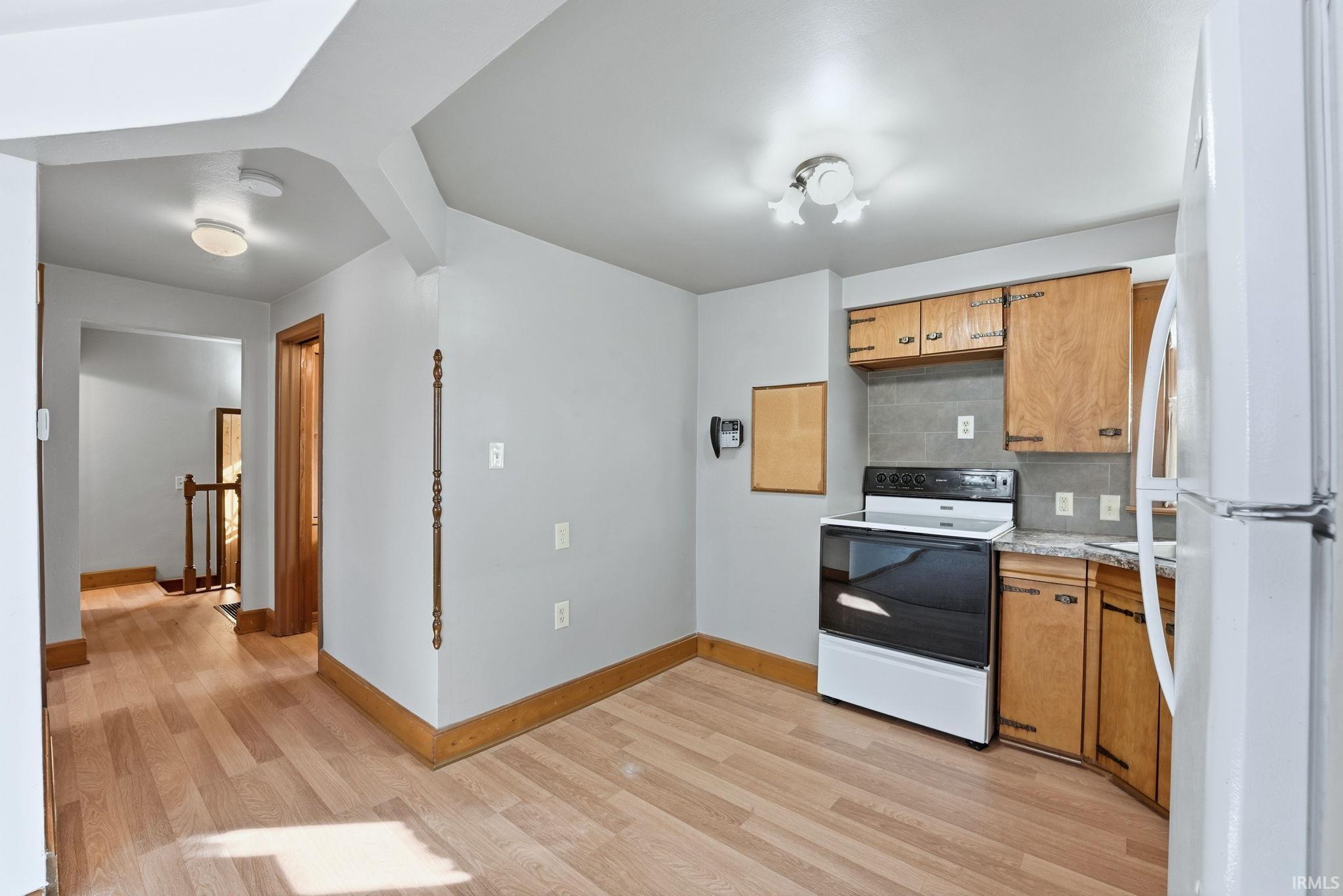 Kitchen featuring freestanding refrigerator, electric range oven, light countertops, backsplash, and light wood finished floors