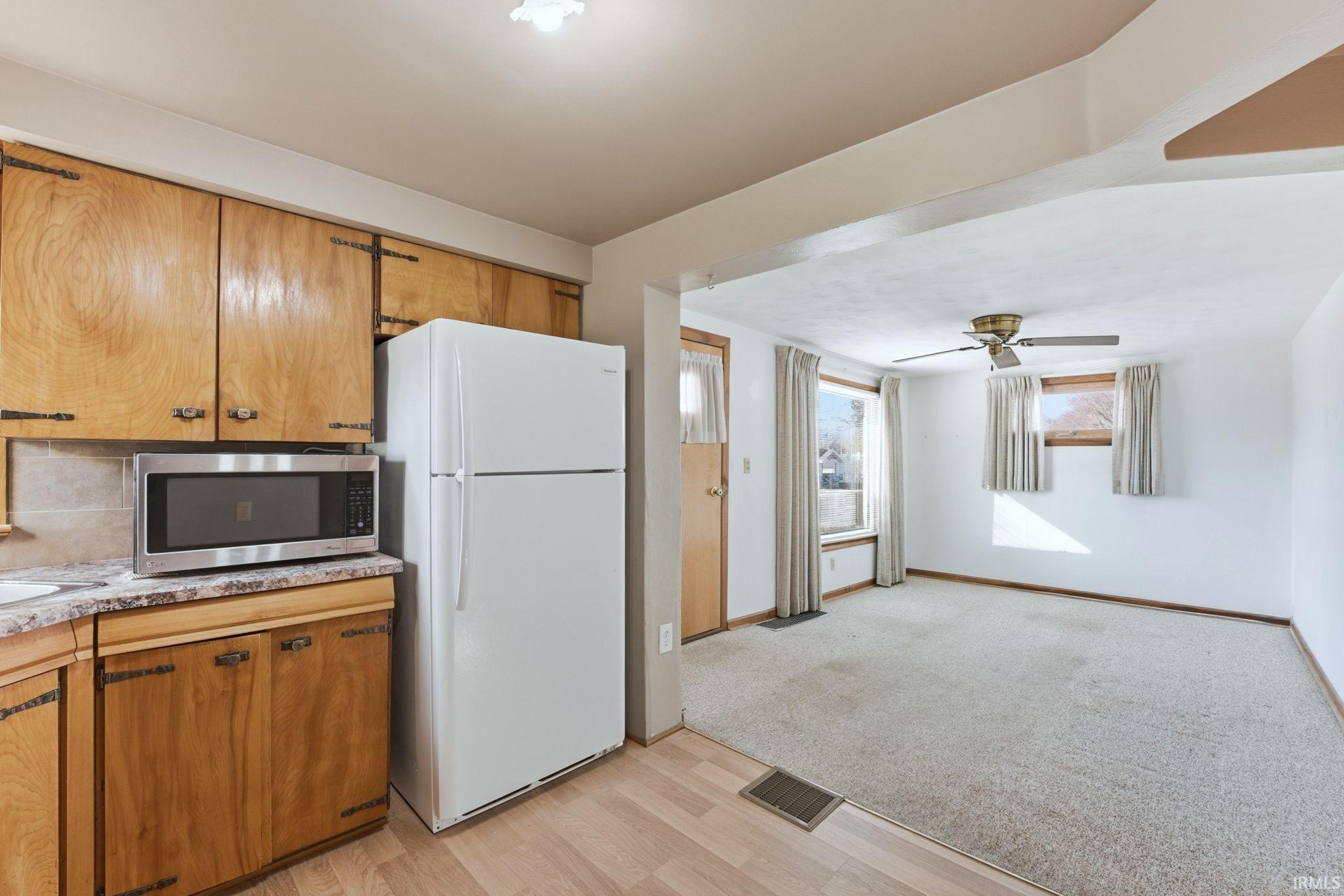 Kitchen featuring freestanding refrigerator, light countertops, stainless steel microwave, wood finish cabinetry, and ceiling fan
