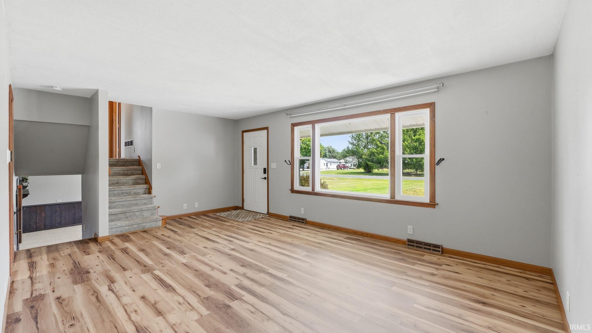 Spacious living area featuring wood-finish flooring, light gray wall paint, and a large front window with wood trim