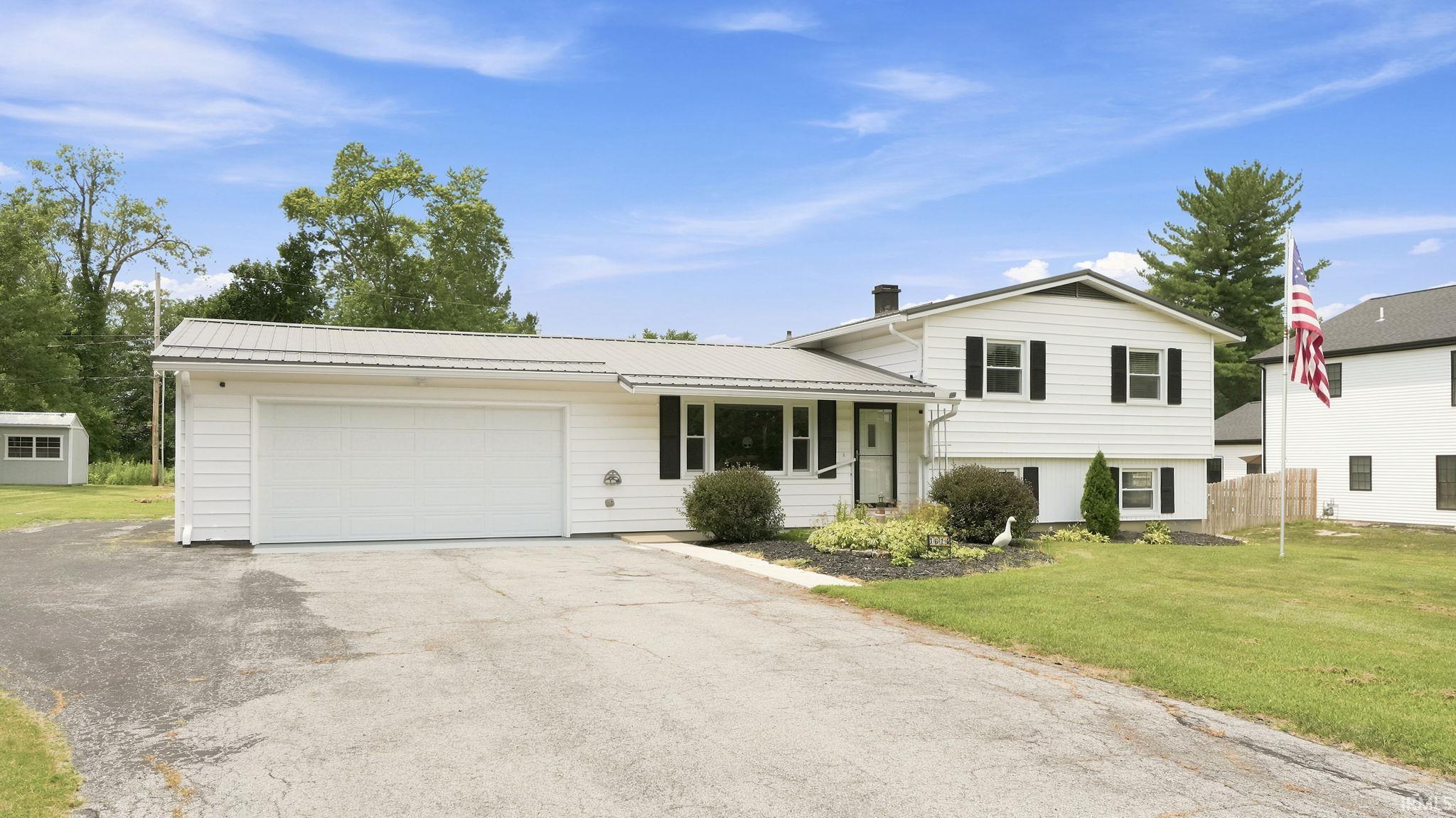 Split-level home featuring white siding, black window shutters, and a prominent attached garage with a white door