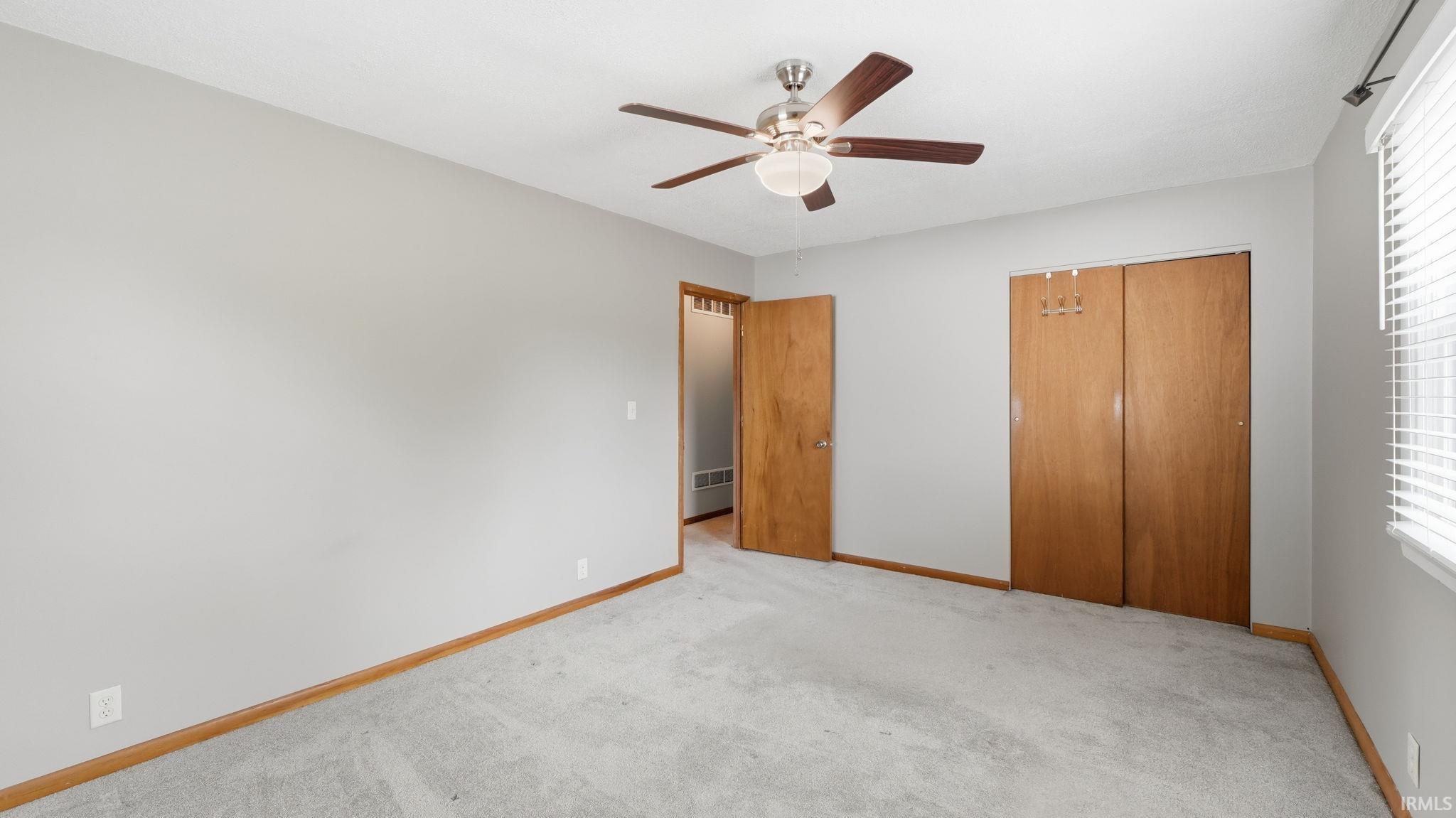 Bedroom featuring neutral wall paint, light-toned carpet, a ceiling fan with integrated lighting, wood-finish baseboards, and a bi-fold closet