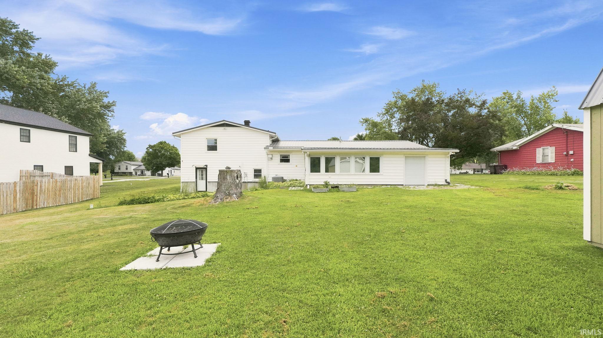 Expansive green lawn with a white two-story residence, featuring a wood fence, mature trees, and a detached shed
