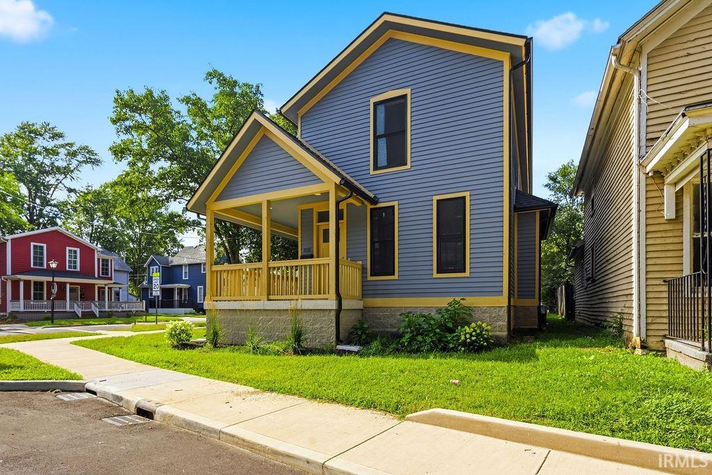 Two-story residence featuring blue horizontal siding with contrasting yellow trim, a covered front porch with natural wood railings, and dark-framed windows