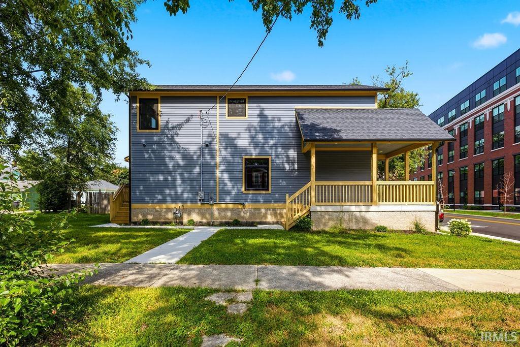 Two-story residence featuring blue siding with yellow trim, a covered front porch with natural wood railings, a gray shingled roof, and a concrete walkway