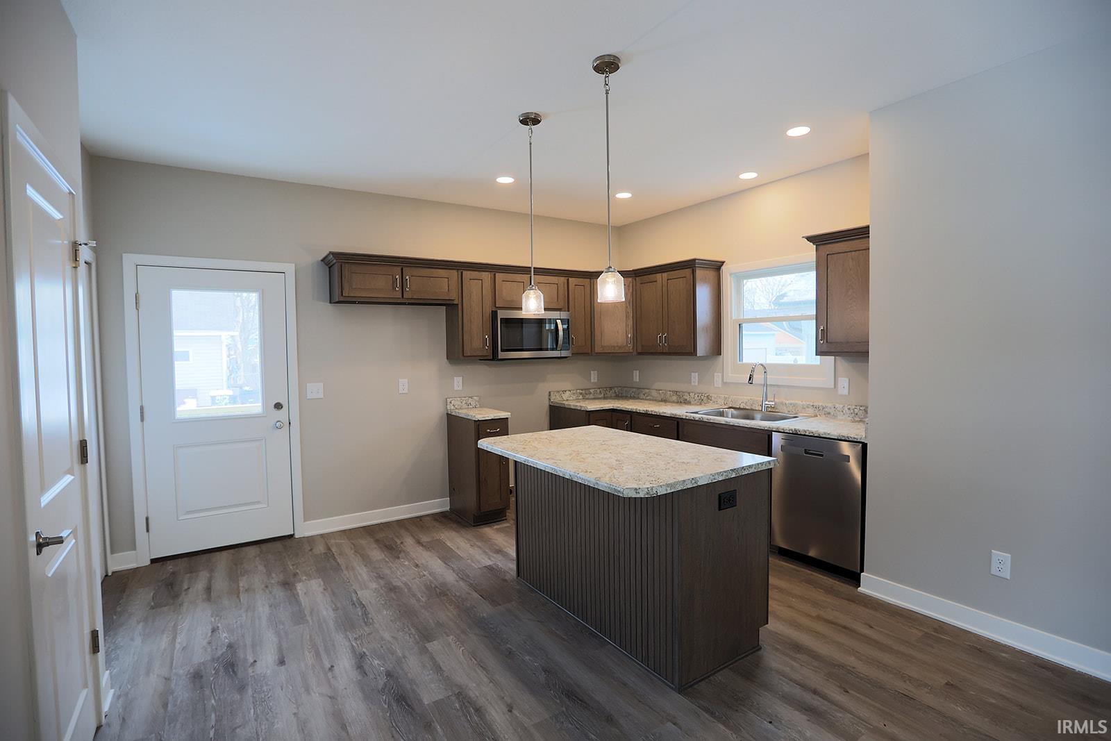 Kitchen featuring decorative light fixtures, stainless steel appliances, dark wood finish cabinets, a kitchen island, and dark wood finished floors