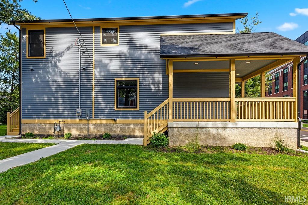 Covered porch with natural wood railings, recessed lighting, and a dark shingle roof