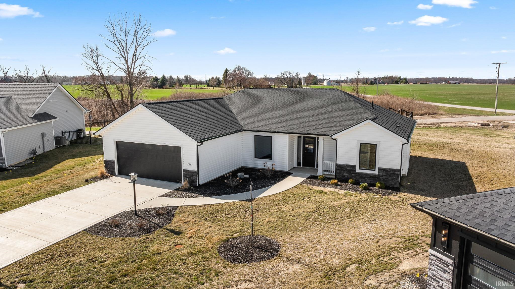 Modern farmhouse style home featuring stone siding, a shingled roof, concrete driveway, and a front lawn