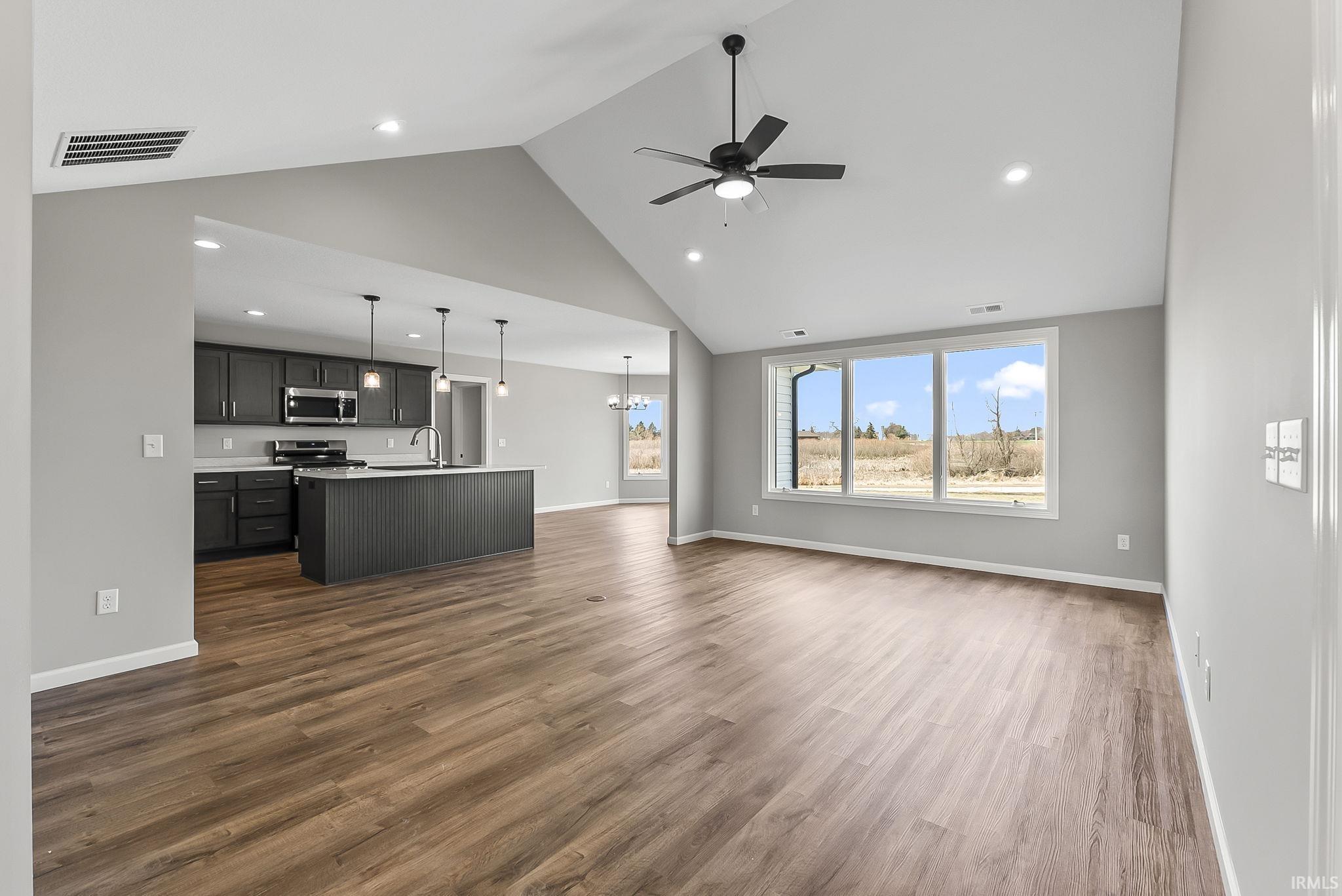 Unfurnished living room with a ceiling fan, a high ceiling, dark wood finished floors, and a chandelier