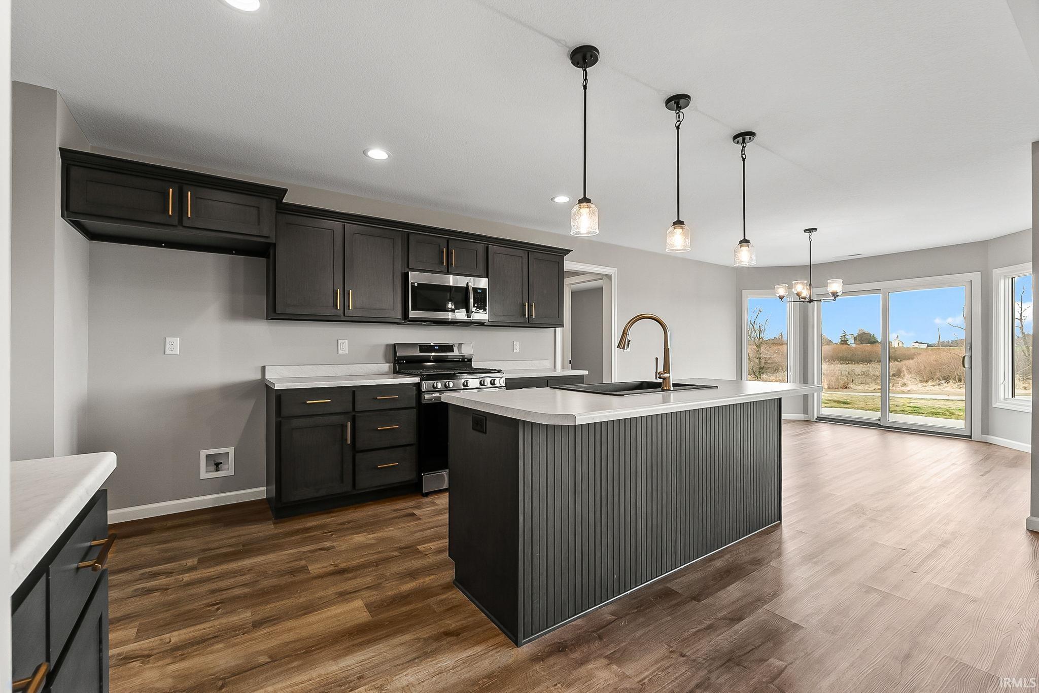 Kitchen featuring light countertops, stainless steel appliances, suspended lighting, and dark wood-style floors