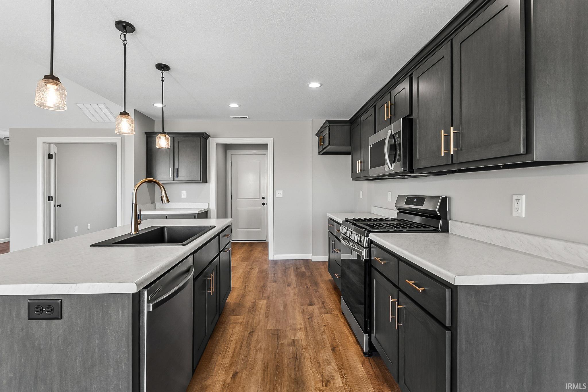 Kitchen featuring stainless steel appliances, a kitchen island with sink, light countertops, and dark wood-type flooring