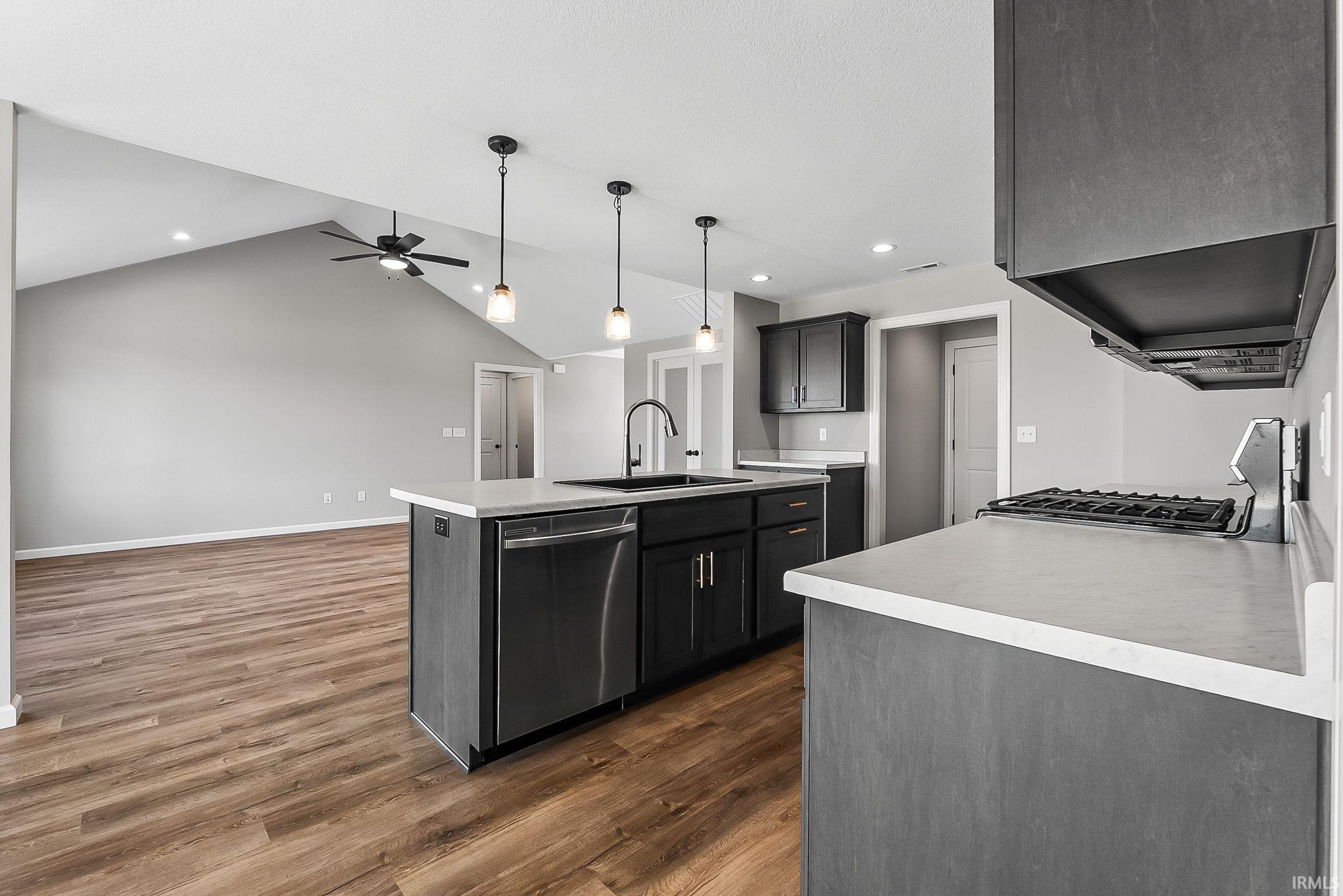 Kitchen featuring light countertops, an island with sink, stainless steel dishwasher, dark wood-style flooring, and range with gas cooktop