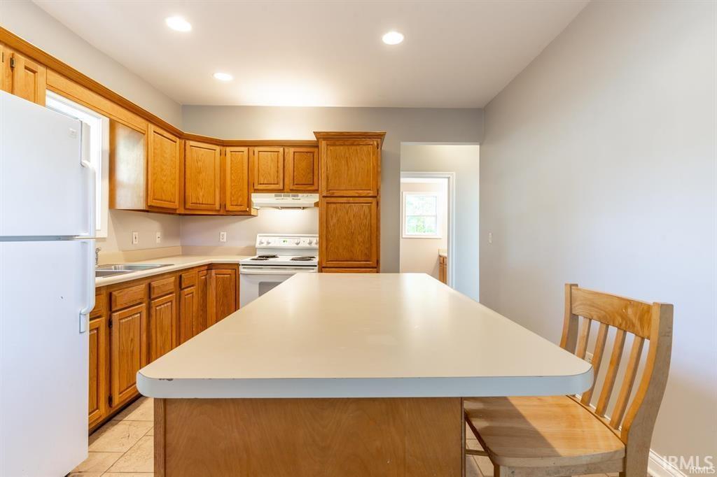 Kitchen featuring white appliances, wood finish cabinetry, light countertops, a kitchen island, and recessed lighting