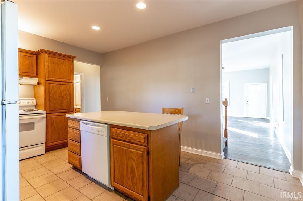 Kitchen with white appliances, wood finish cabinetry, light tile patterned flooring, light countertops, and a kitchen island
