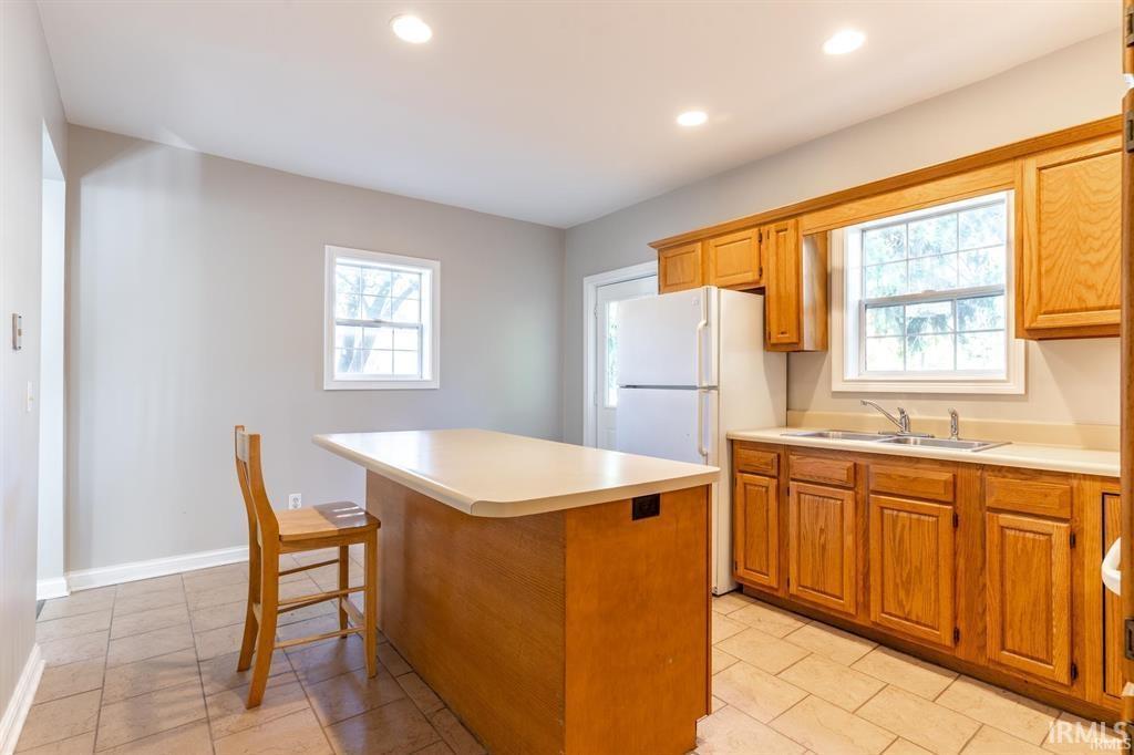 Kitchen with a center island, wood finish cabinetry, light countertops, recessed lighting, and freestanding refrigerator