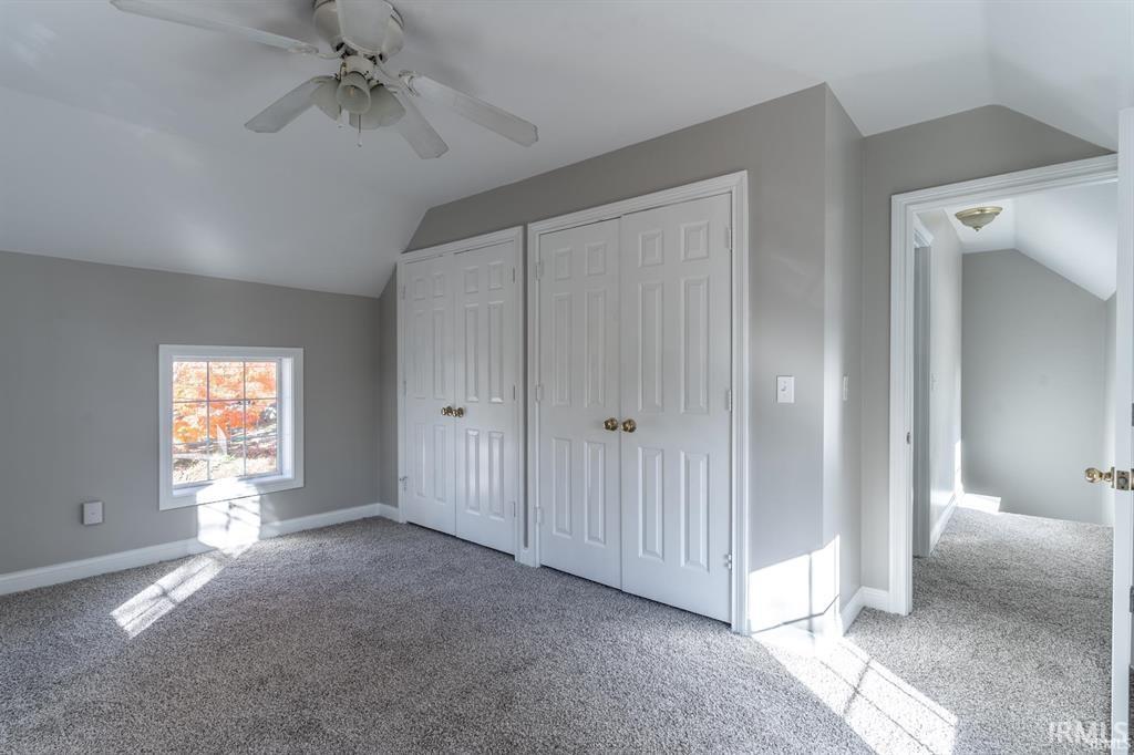 Unfurnished bedroom featuring lofted ceiling, light colored carpet, multiple closets, and a ceiling fan