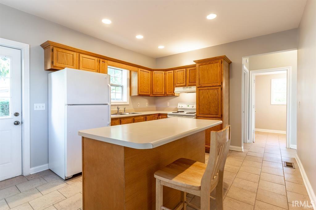 Kitchen with white appliances, wood finish cabinets, light countertops, a breakfast bar, and recessed lighting