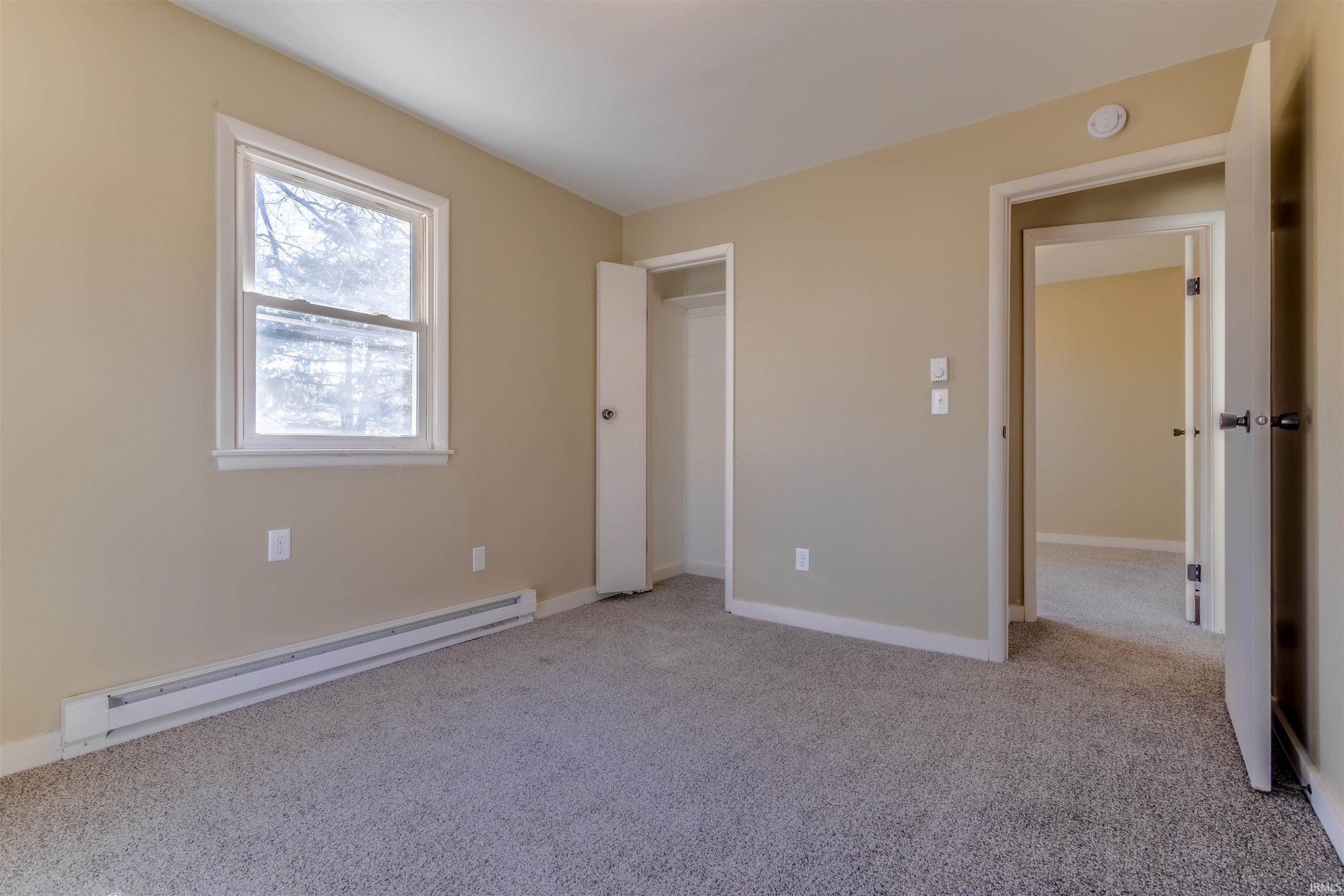 Unfurnished bedroom with a baseboard radiator and light carpet