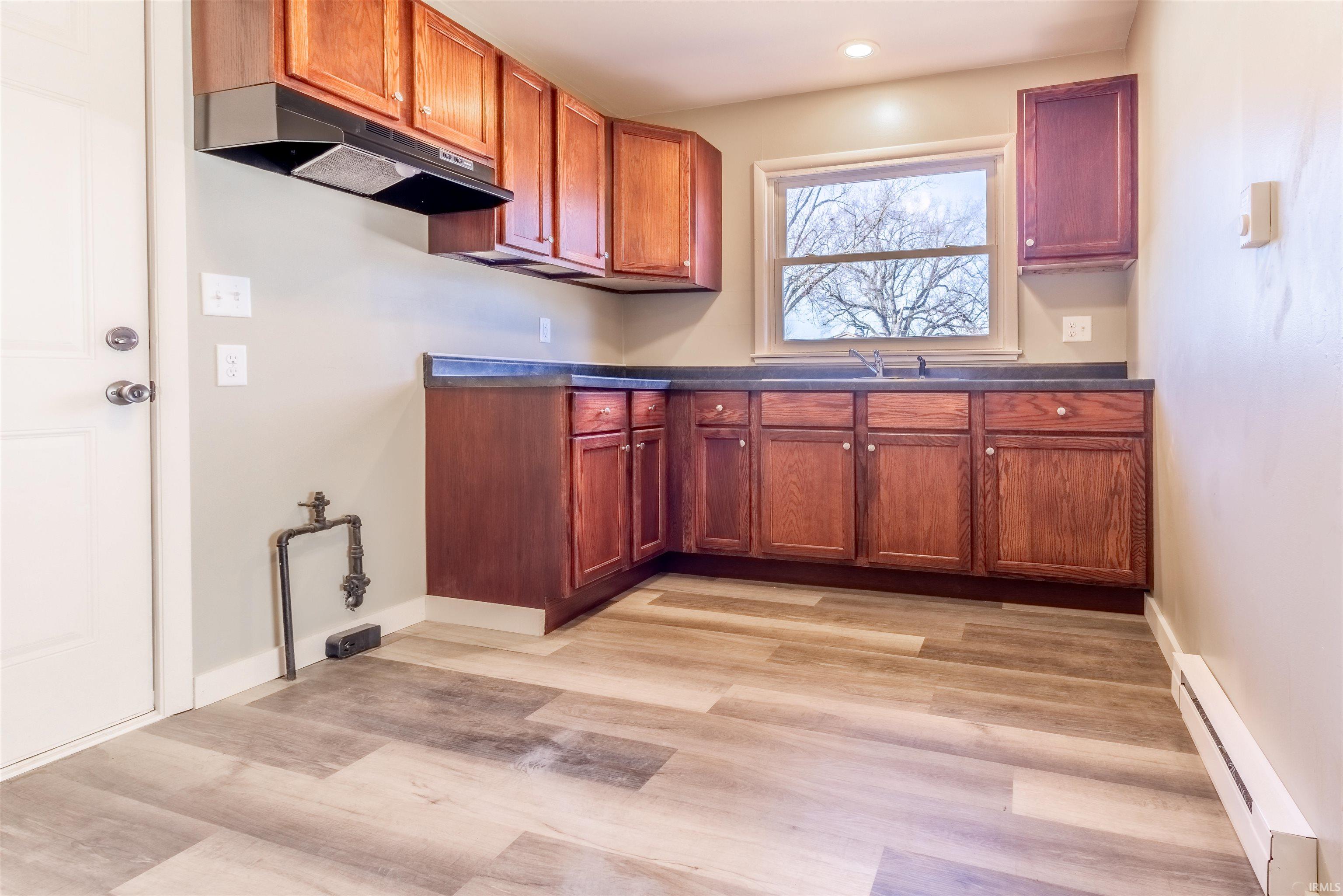 Kitchen featuring a baseboard heating unit, dark countertops, light wood finished floors, recessed lighting, and wood finish cabinets