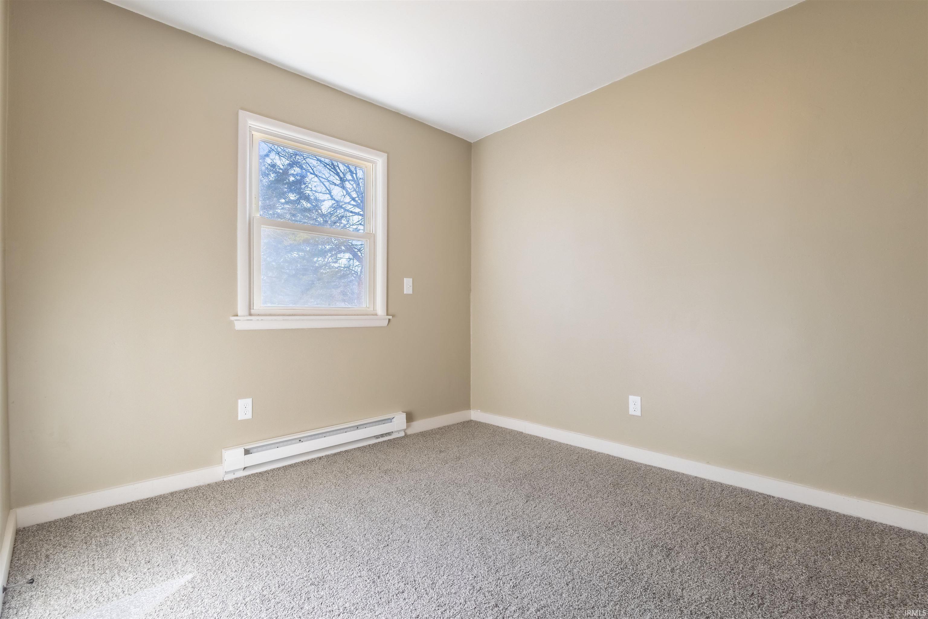 Carpeted empty room with a baseboard radiator and baseboards