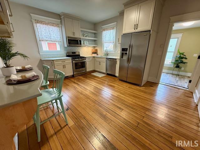 Kitchen with open shelves, appliances with stainless steel finishes, light wood finished floors, and backsplash