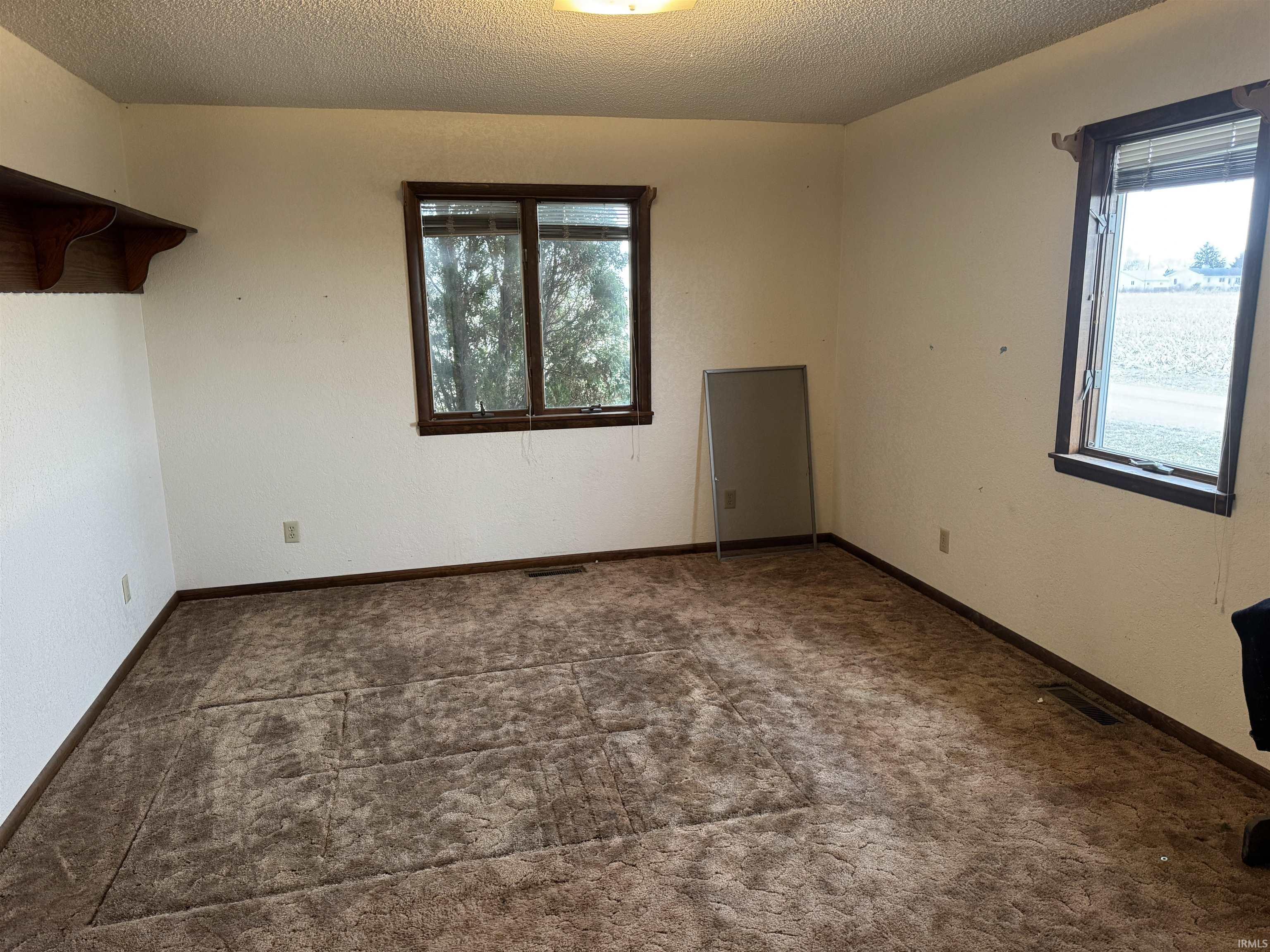 Empty room with a textured ceiling and dark colored carpet
