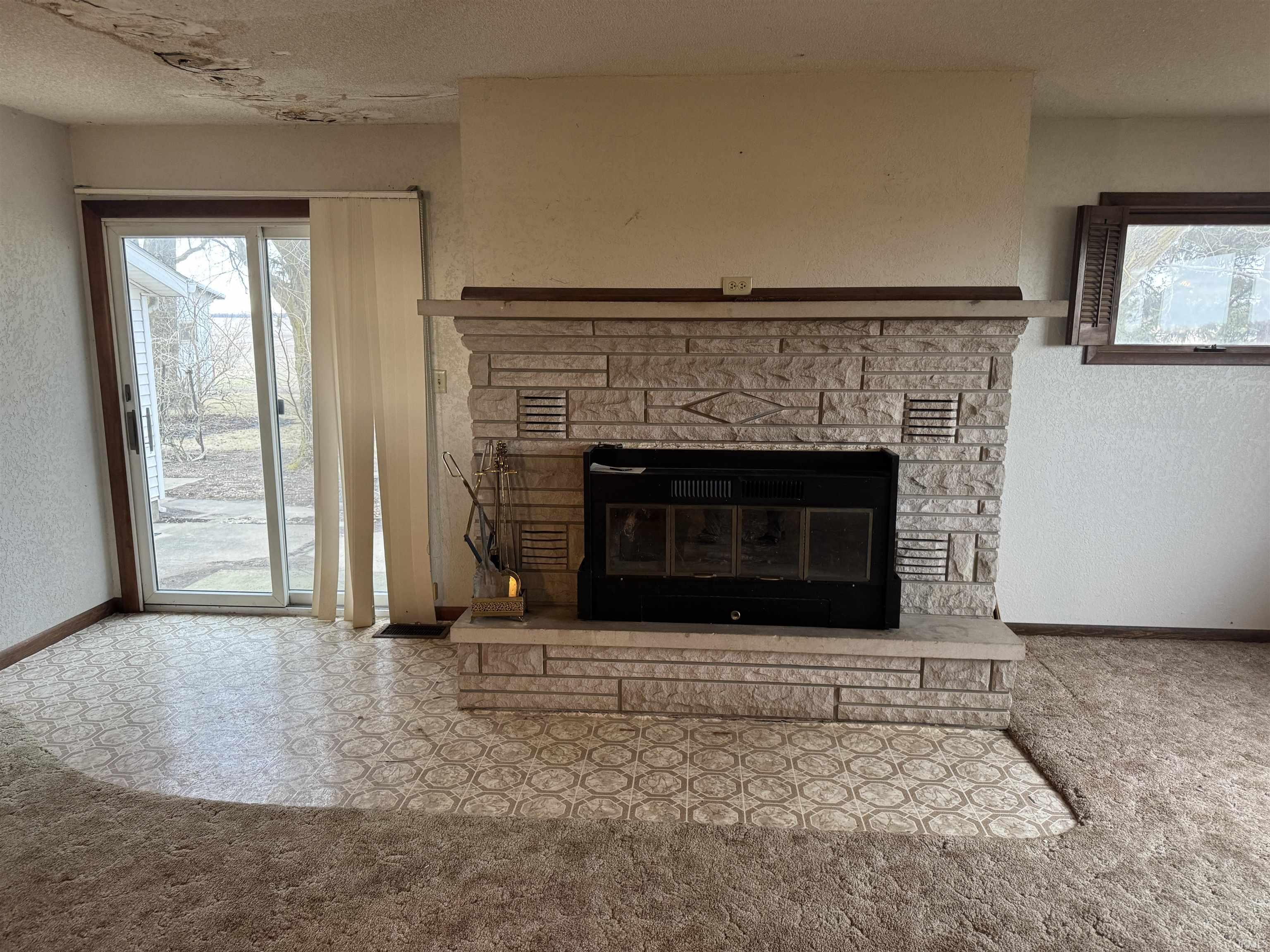 Detailed view of a textured wall, a stone fireplace, a textured ceiling, and carpet flooring