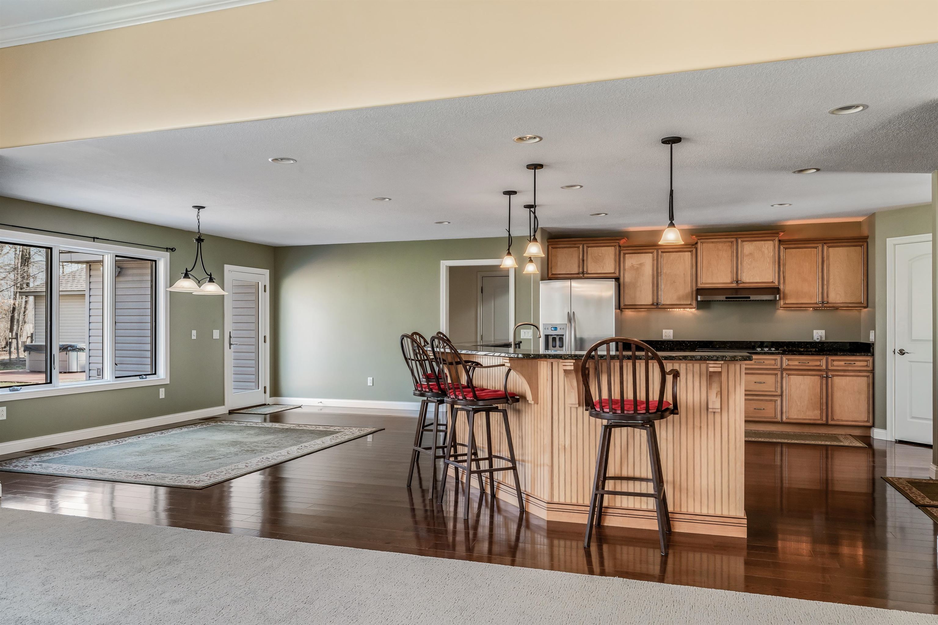 Kitchen with a breakfast bar, wood finish cabinetry, stainless steel fridge, hanging light fixtures, and a center island with sink