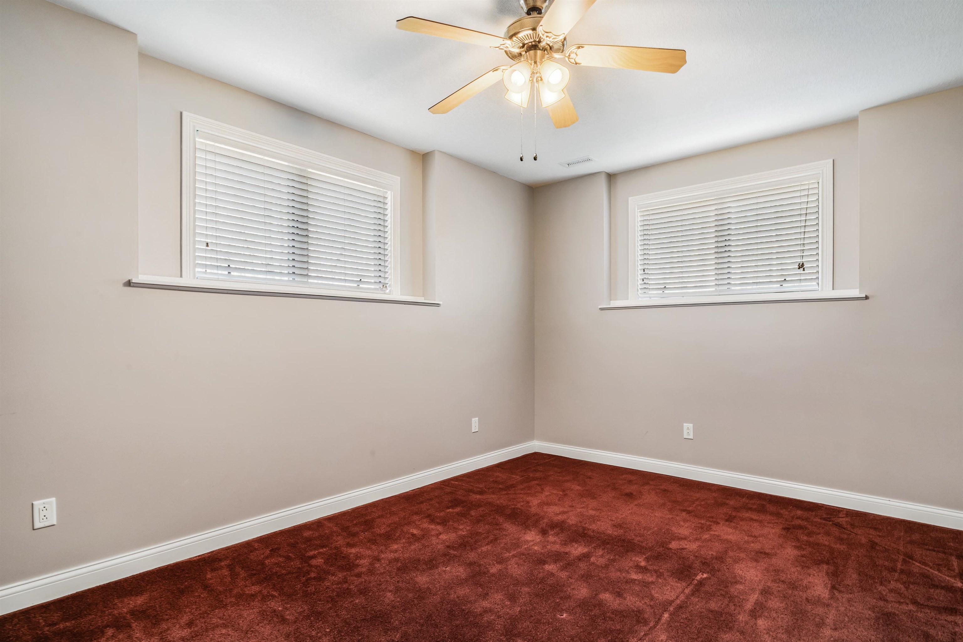 Empty room featuring dark colored carpet, ceiling fan, and healthy amount of natural light