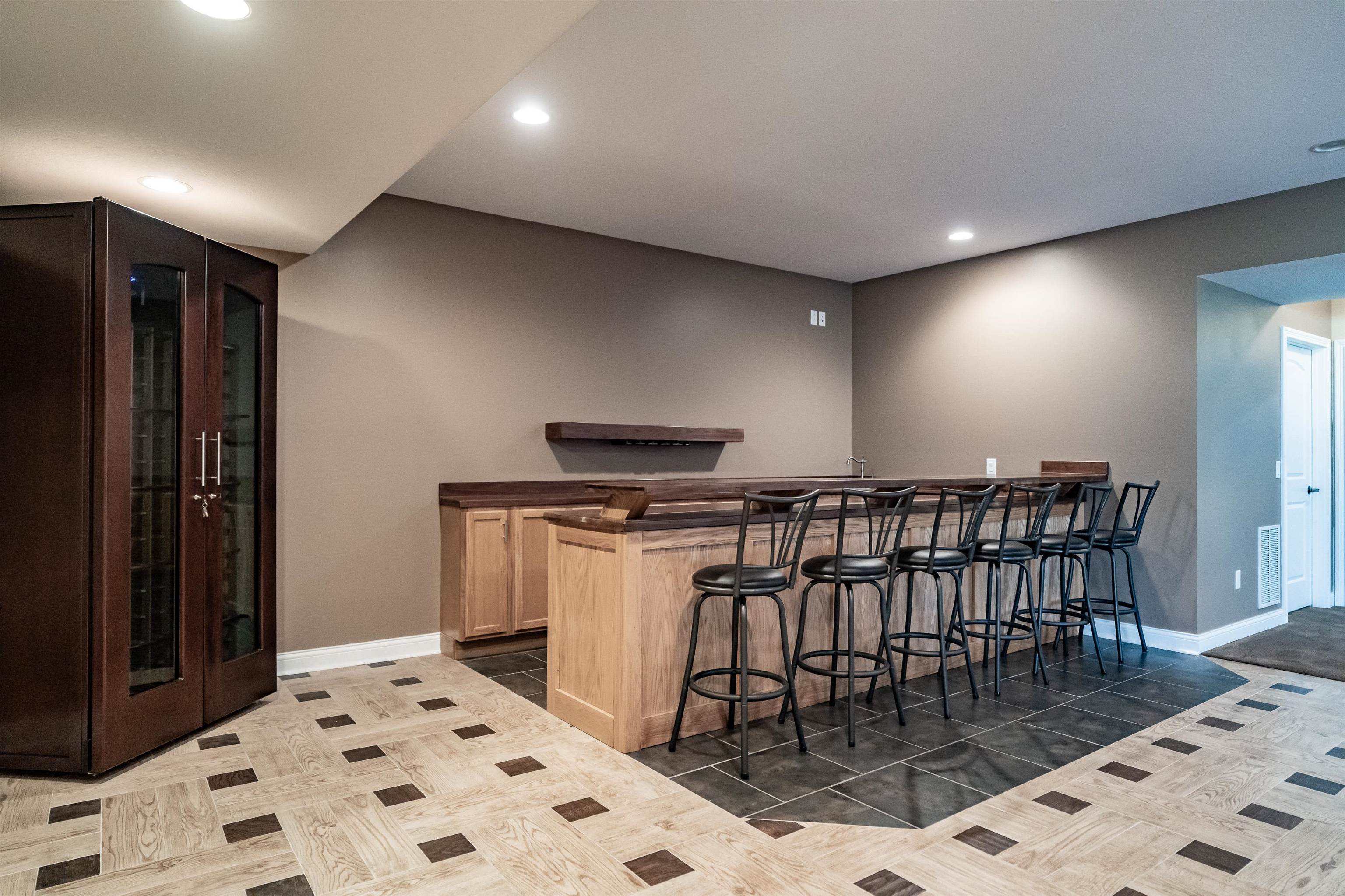 Indoor wet bar featuring dark countertops, recessed lighting, glass fronted cabinets, and light wood finish cabinets