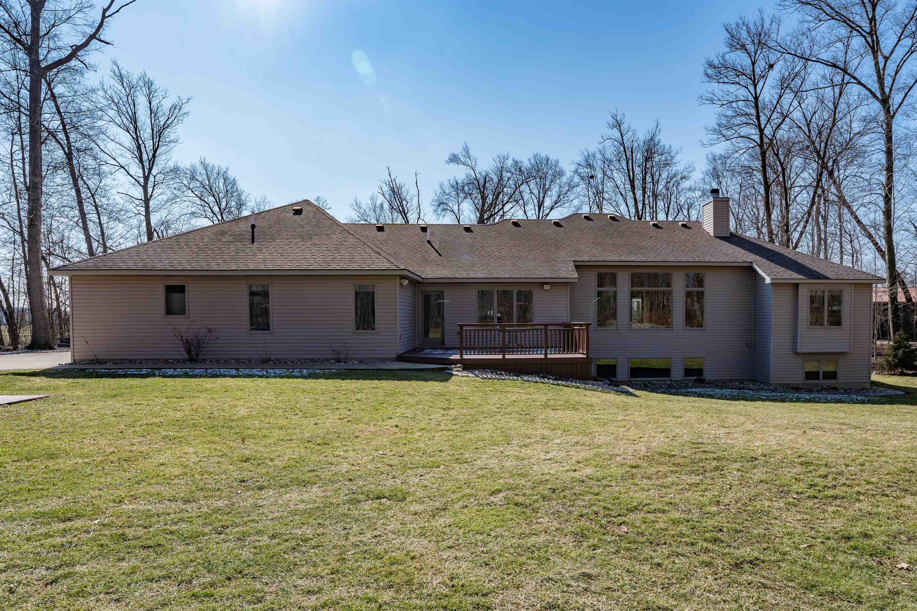 Back of house featuring a wooden deck, roof with shingles, and a lawn