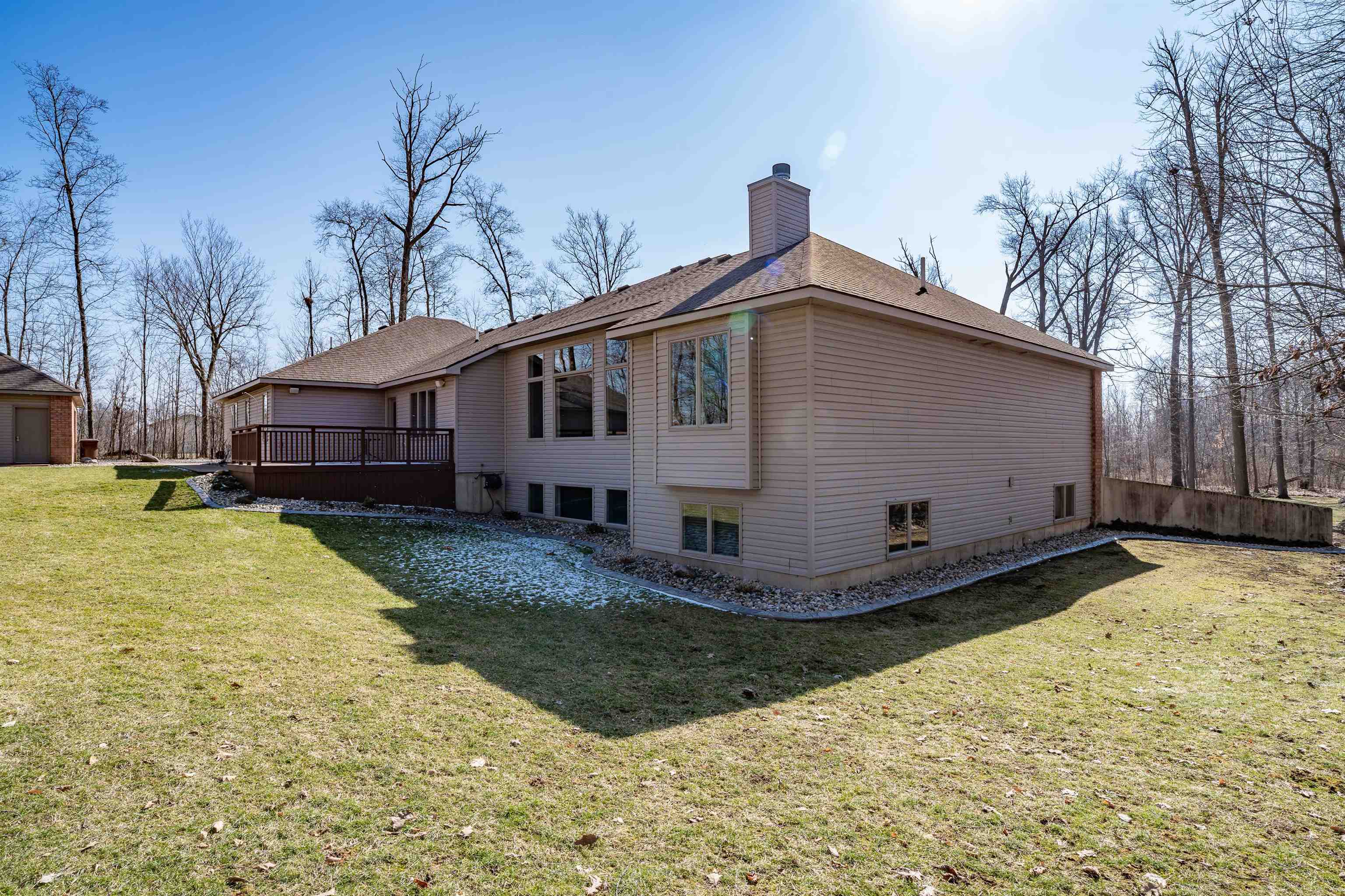 Back of house featuring a yard, a wooden deck, a chimney, and a shingled roof