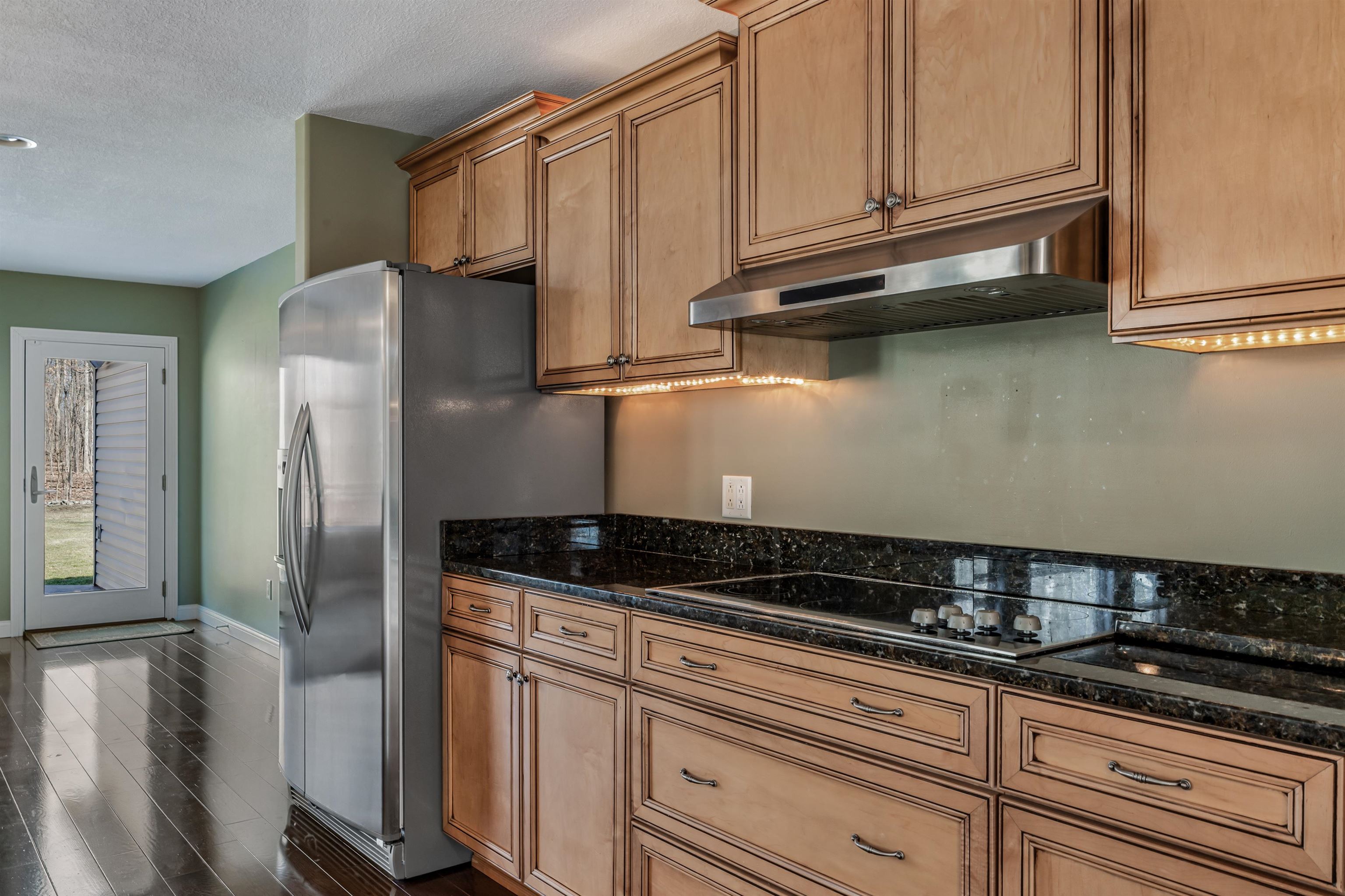 Kitchen featuring dark stone countertops, a textured ceiling, stainless steel refrigerator with ice dispenser, black electric cooktop, and dark wood-type flooring