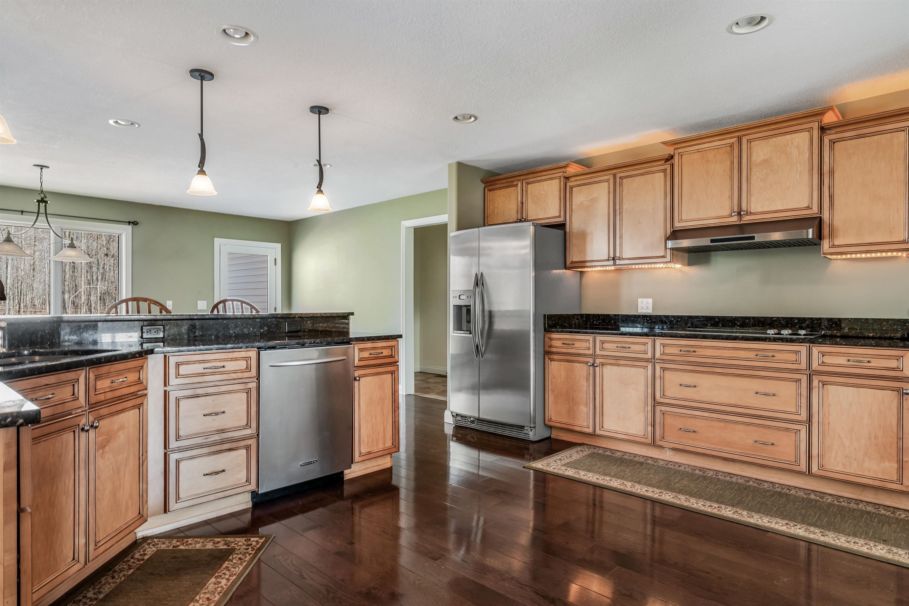 Kitchen featuring dark stone countertops, dark wood-style floors, stainless steel appliances, decorative light fixtures, and wood finish cabinetry