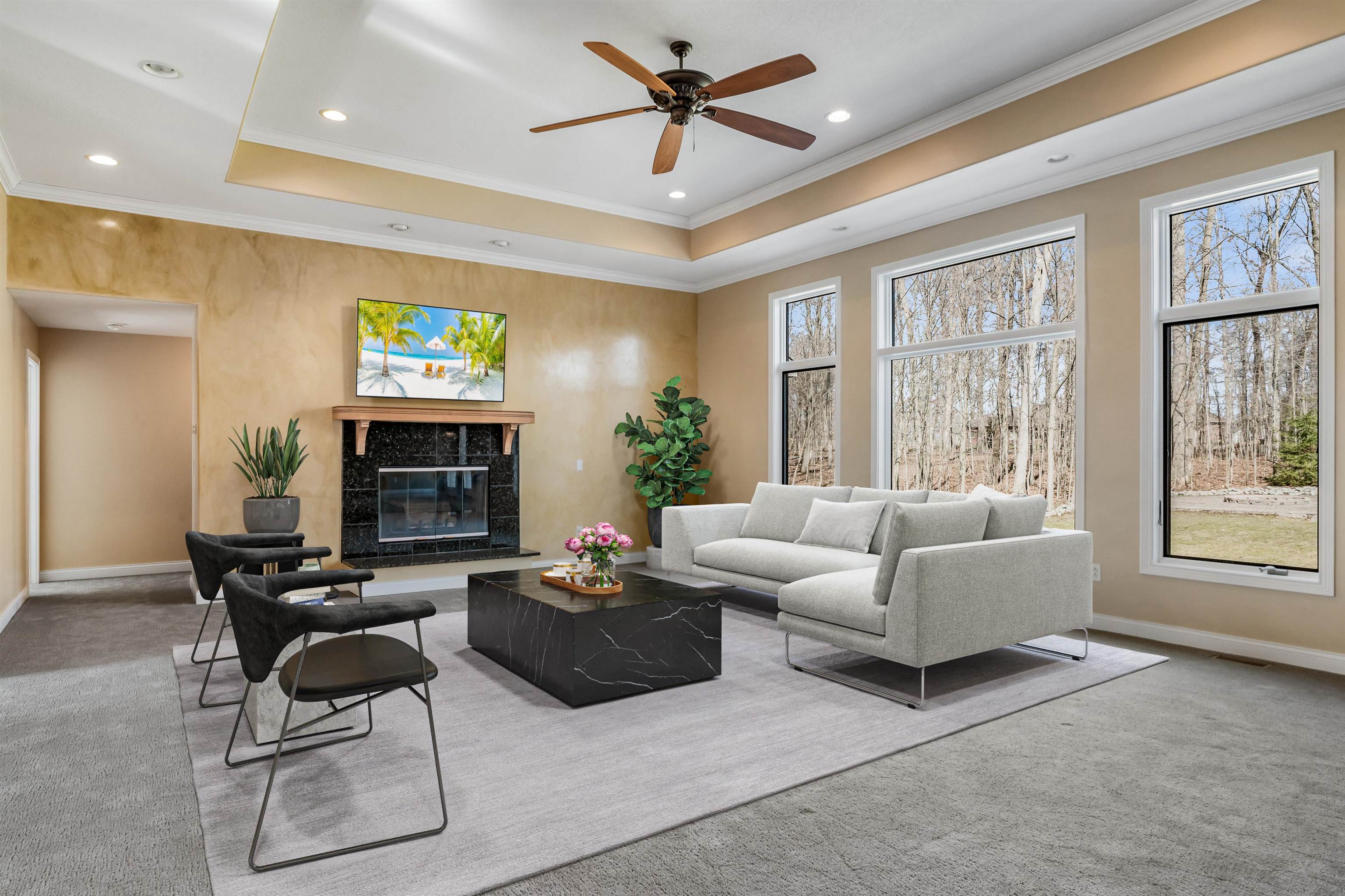 Living area featuring light carpet, a ceiling fan, a premium fireplace, ornamental molding, and a tray ceiling