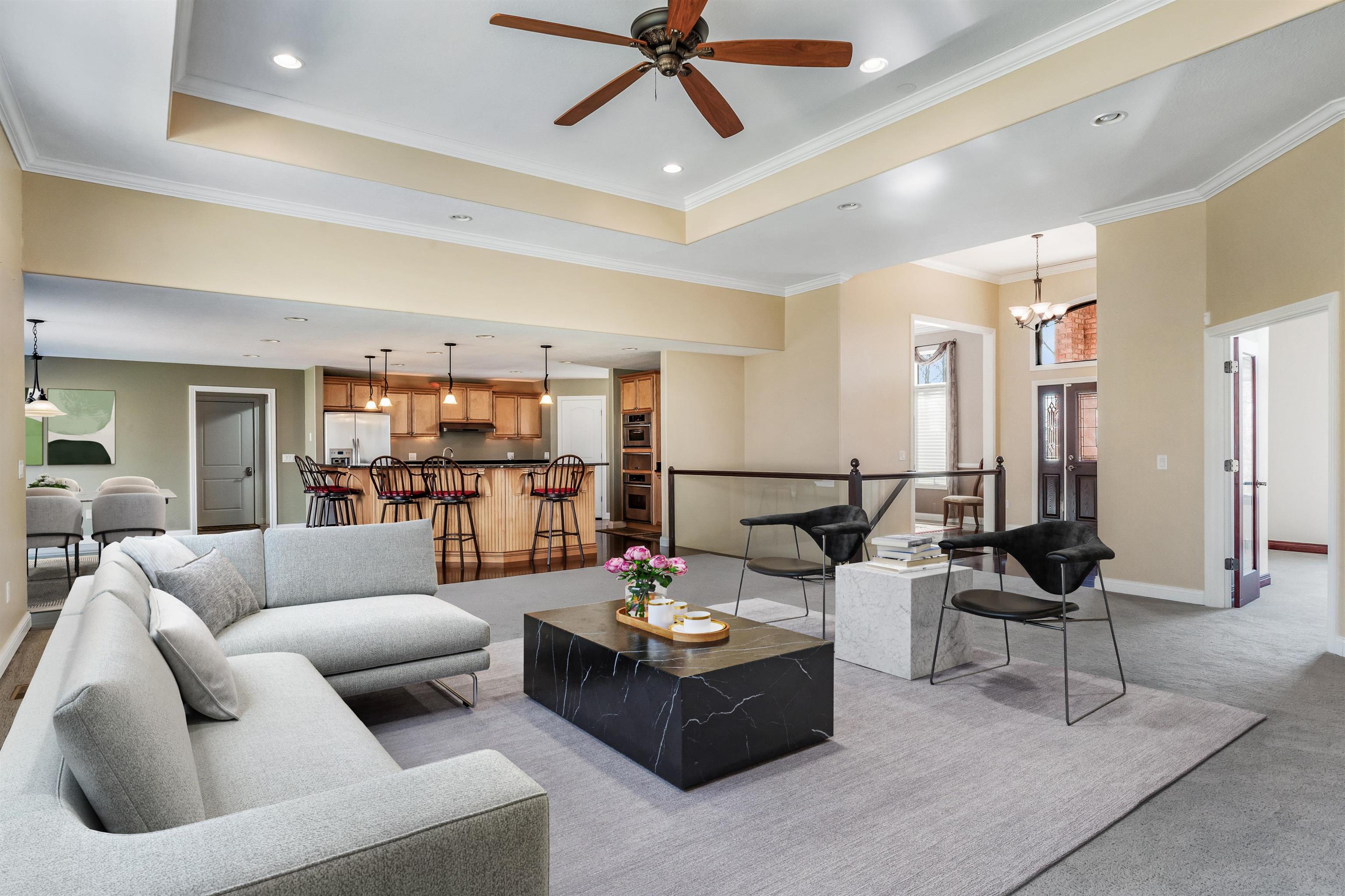 Living room with a ceiling fan, light colored carpet, a raised ceiling, ornamental molding, and suspended lighting
