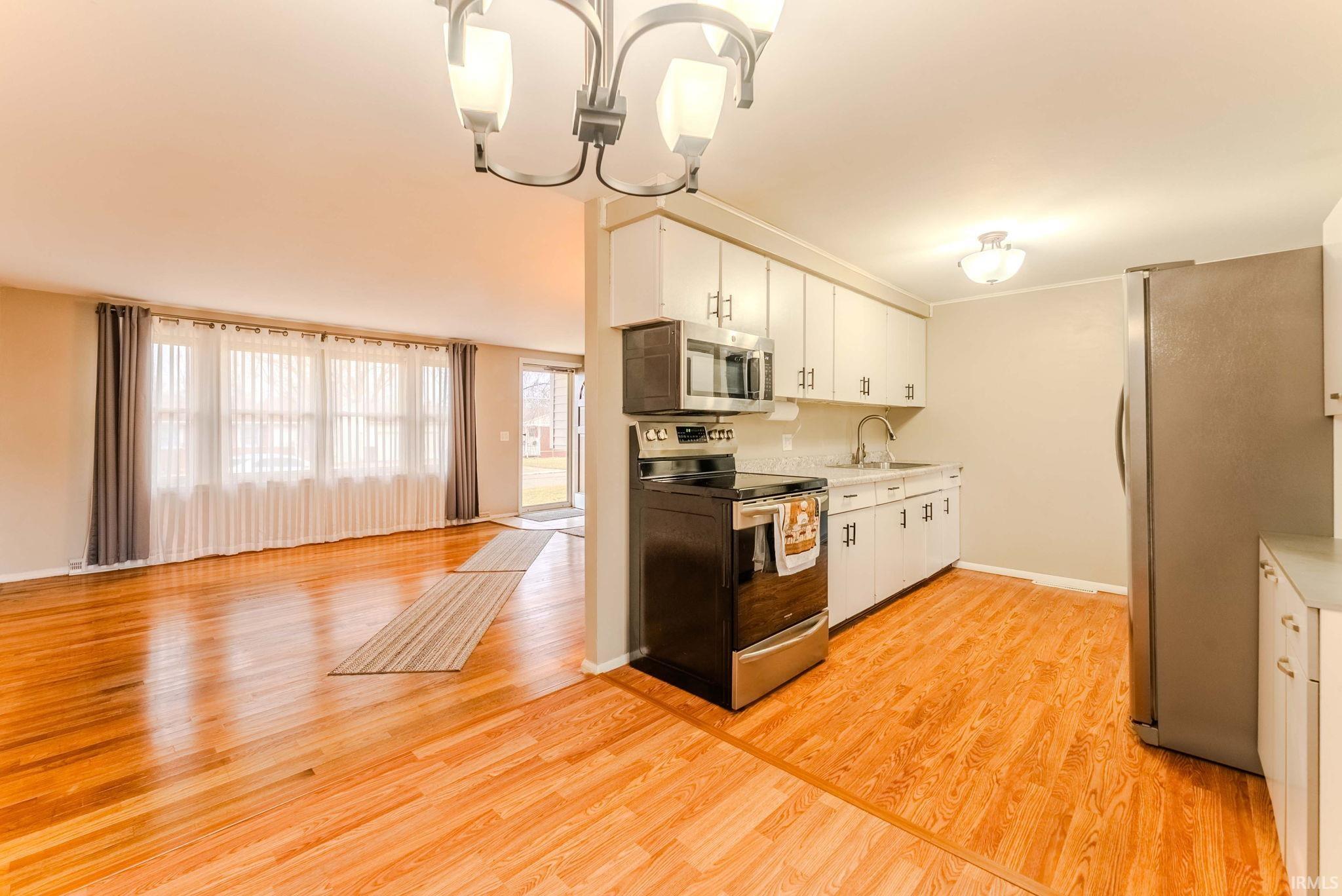 Kitchen with stainless steel appliances, light countertops, white cabinets, light wood-type flooring, and suspended lighting