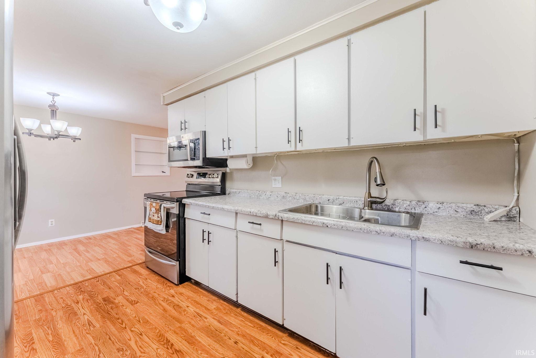 Kitchen with stainless steel appliances, light wood-type flooring, white cabinetry, and a chandelier