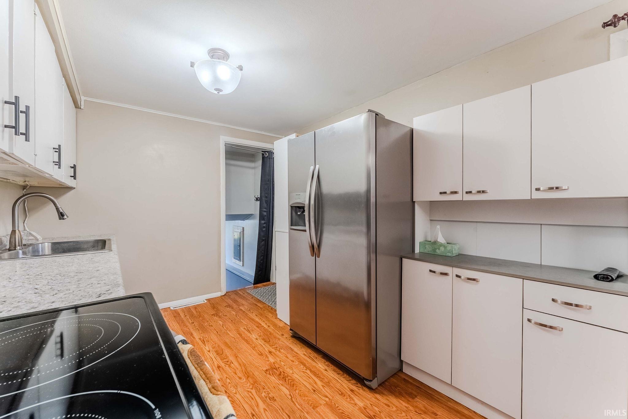 Kitchen with stainless steel fridge with ice dispenser, white cabinets, light wood-type flooring, black range with electric cooktop, and crown molding
