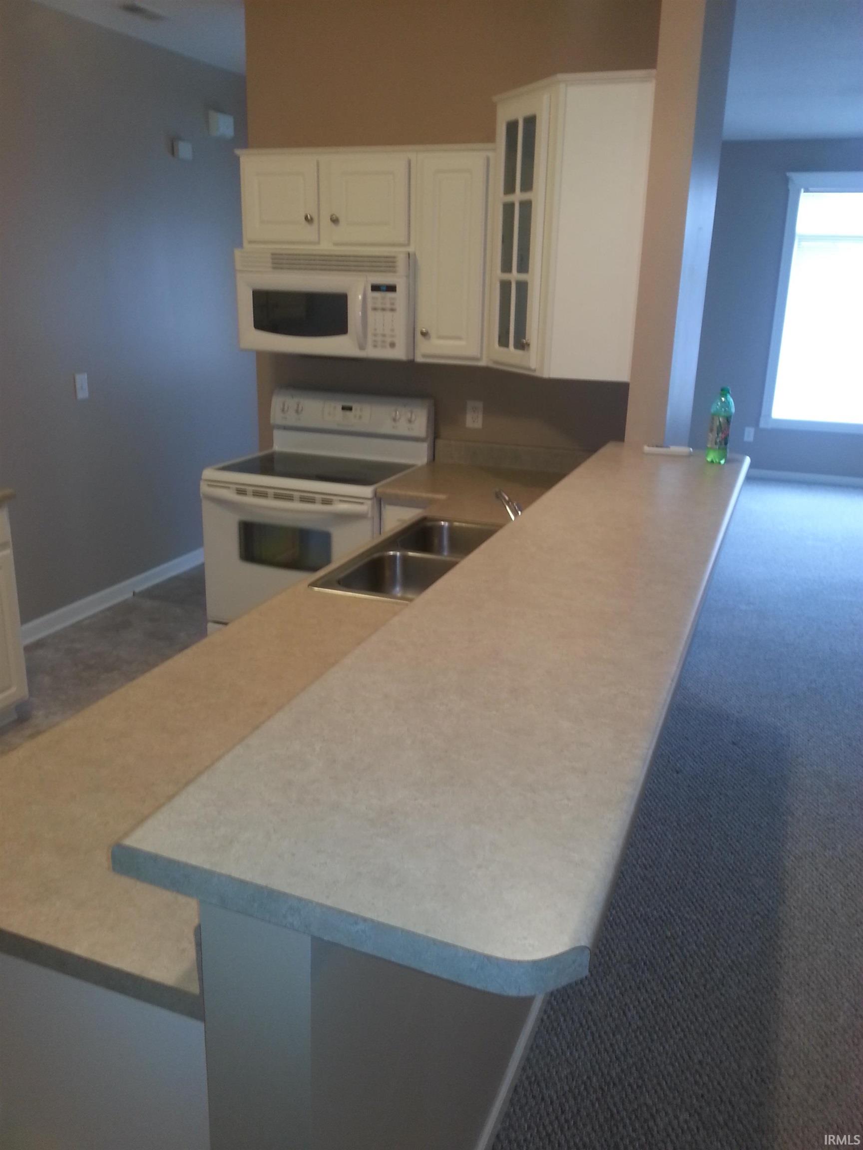 Kitchen with glass fronted cabinets, white appliances, light countertops, and dark carpet