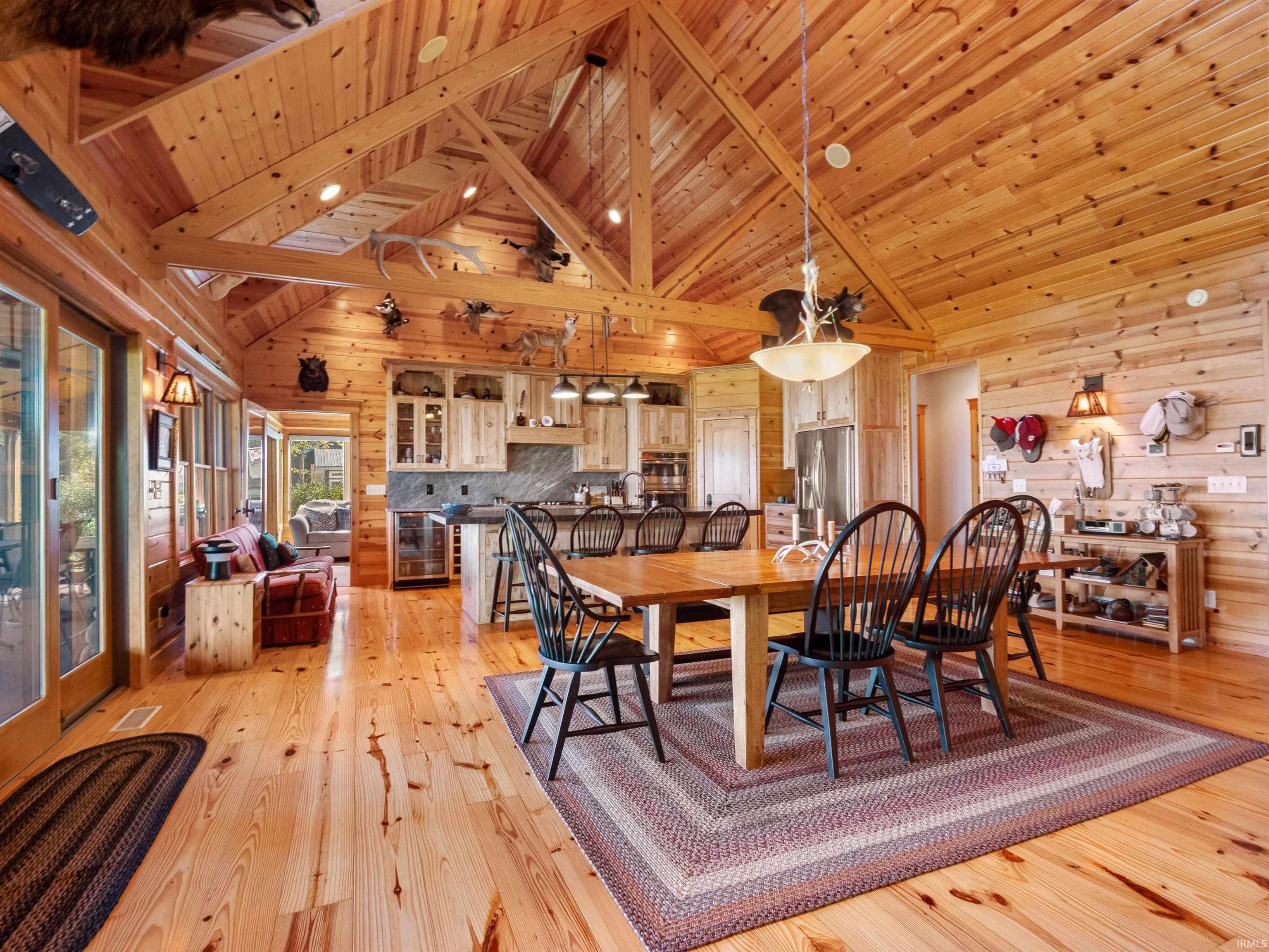 Dining room with beverage cooler, a high wood beamed ceiling, light wood finished floors, and wooden walls