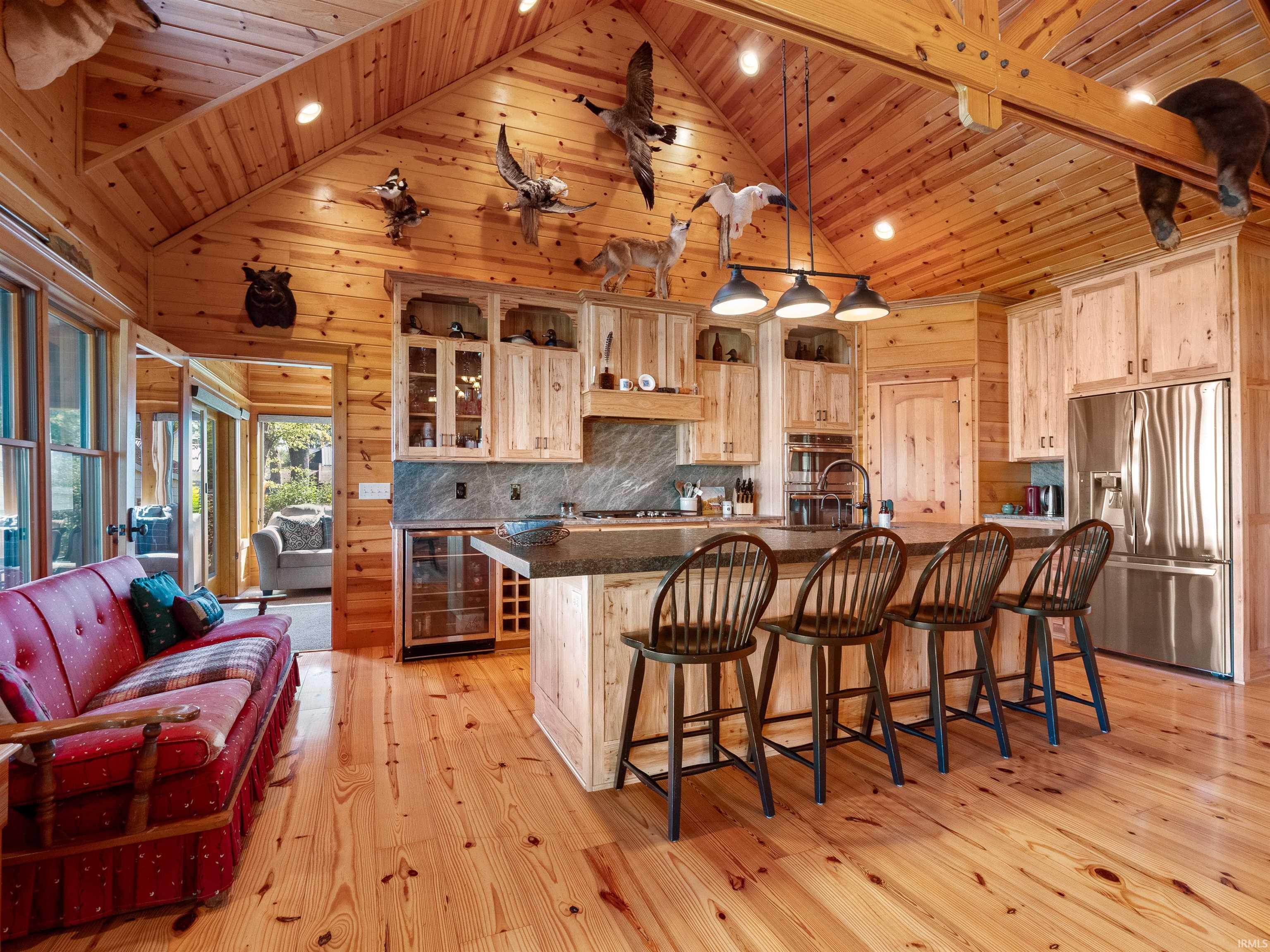 Kitchen featuring glass insert cabinets, light wood-style flooring, stainless steel fridge, a kitchen bar, and wine cooler