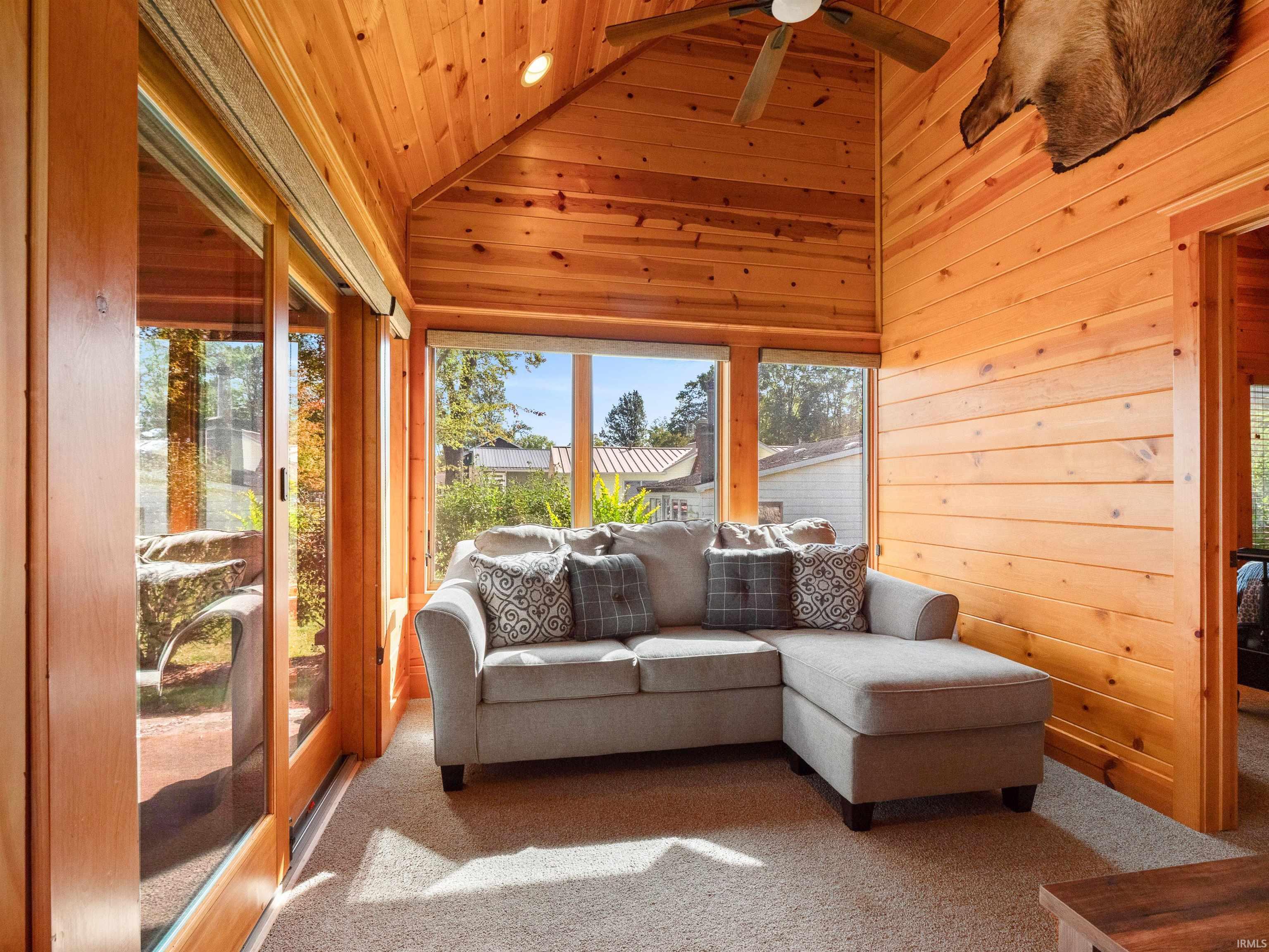 Sunroom / solarium featuring carpet flooring, wood walls, and a vaulted wooden ceiling