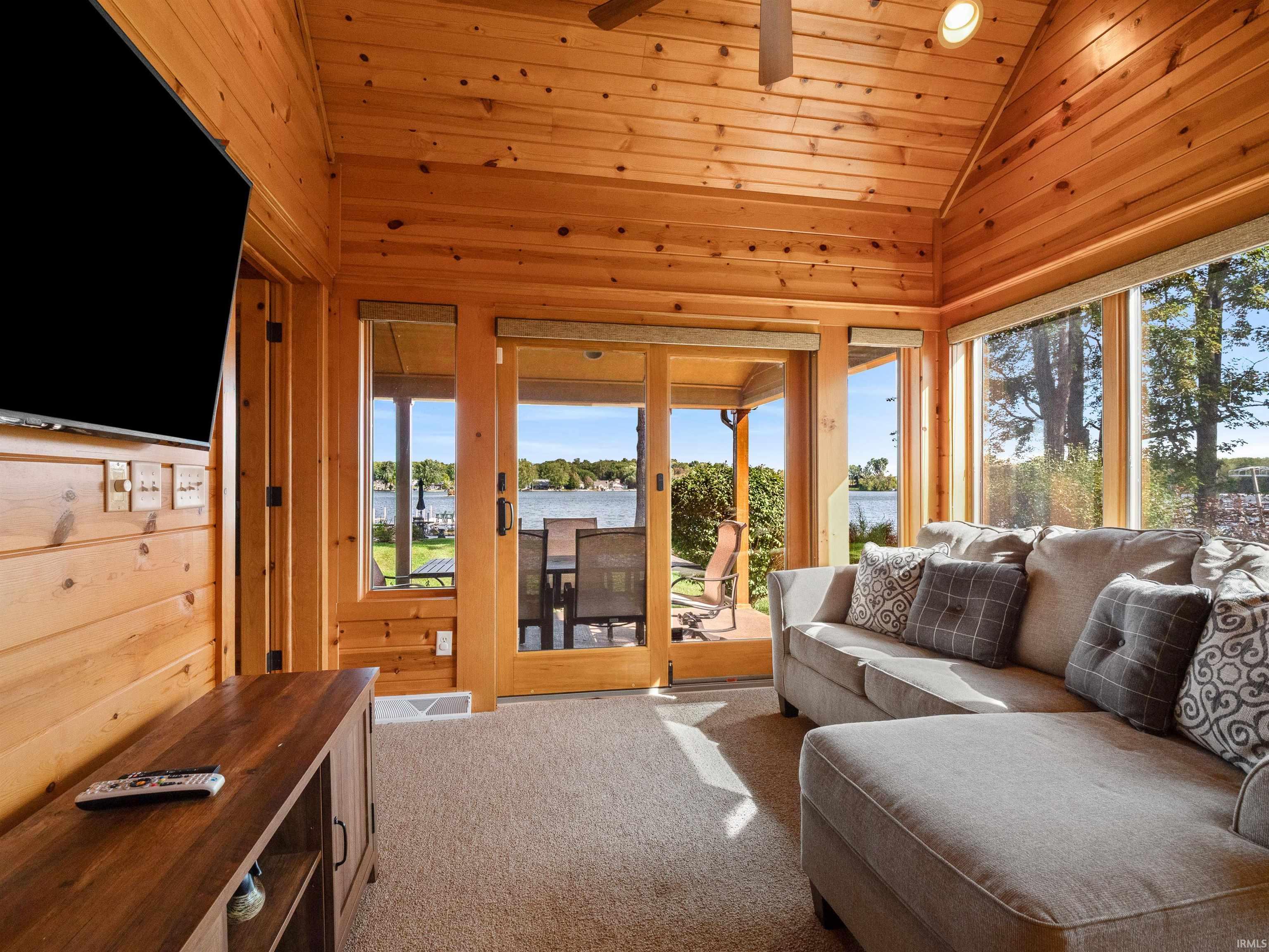 Living room with wood walls, a vaulted wood ceiling, carpet flooring, a ceiling fan, and a water view