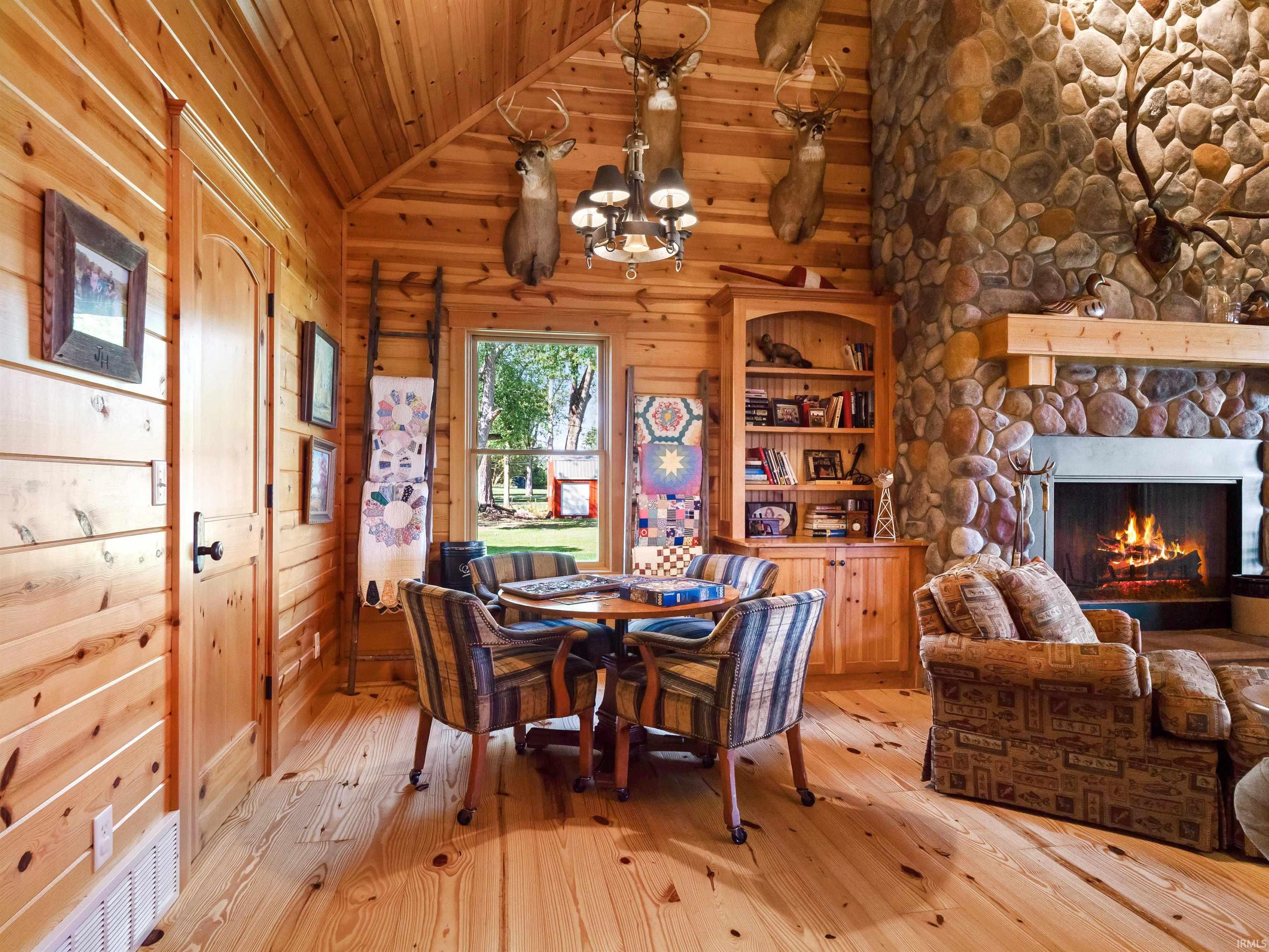 Dining area with light wood-type flooring, a stone fireplace, a vaulted wooden ceiling, hanging lights, and wooden walls