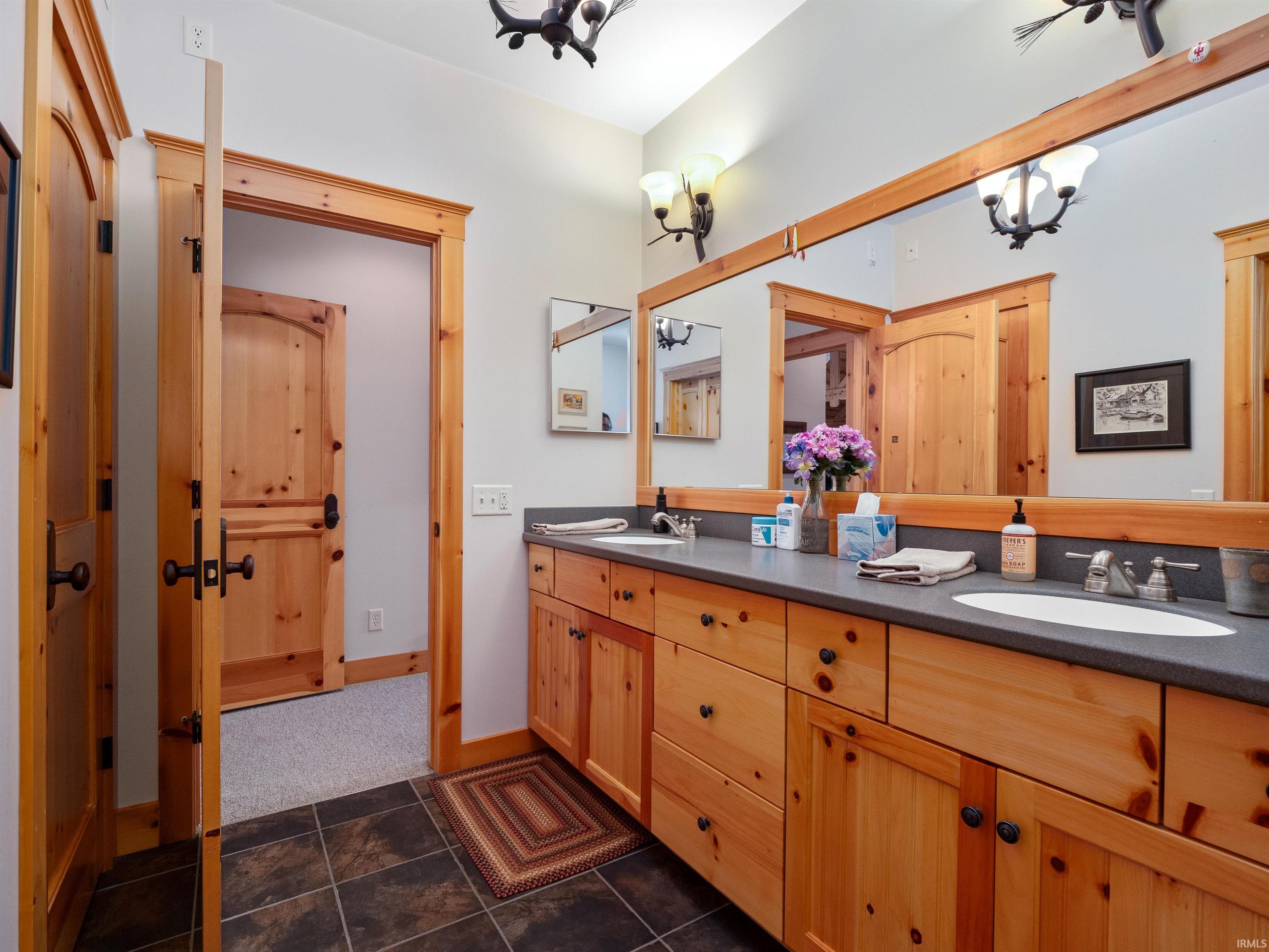 Bathroom featuring double vanity, dark tile patterned flooring, and suspended lighting